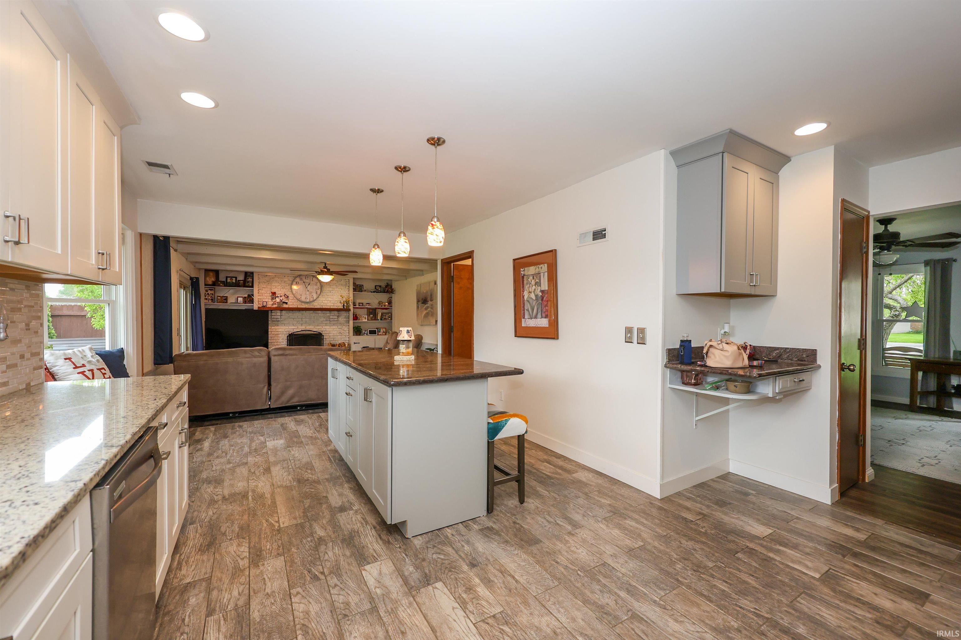 Kitchen featuring wood-finish flooring, a central island with a stone countertop, pendant lighting, white cabinetry, and a stainless steel dishwasher