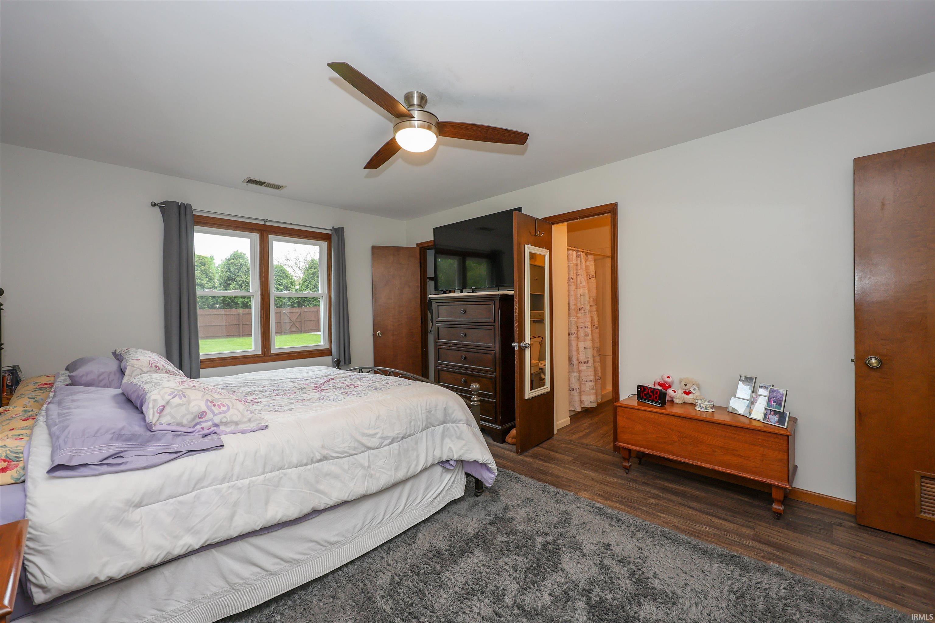 Bedroom featuring wood-finish flooring, a ceiling fan with integrated lighting, and a large window with wood trim