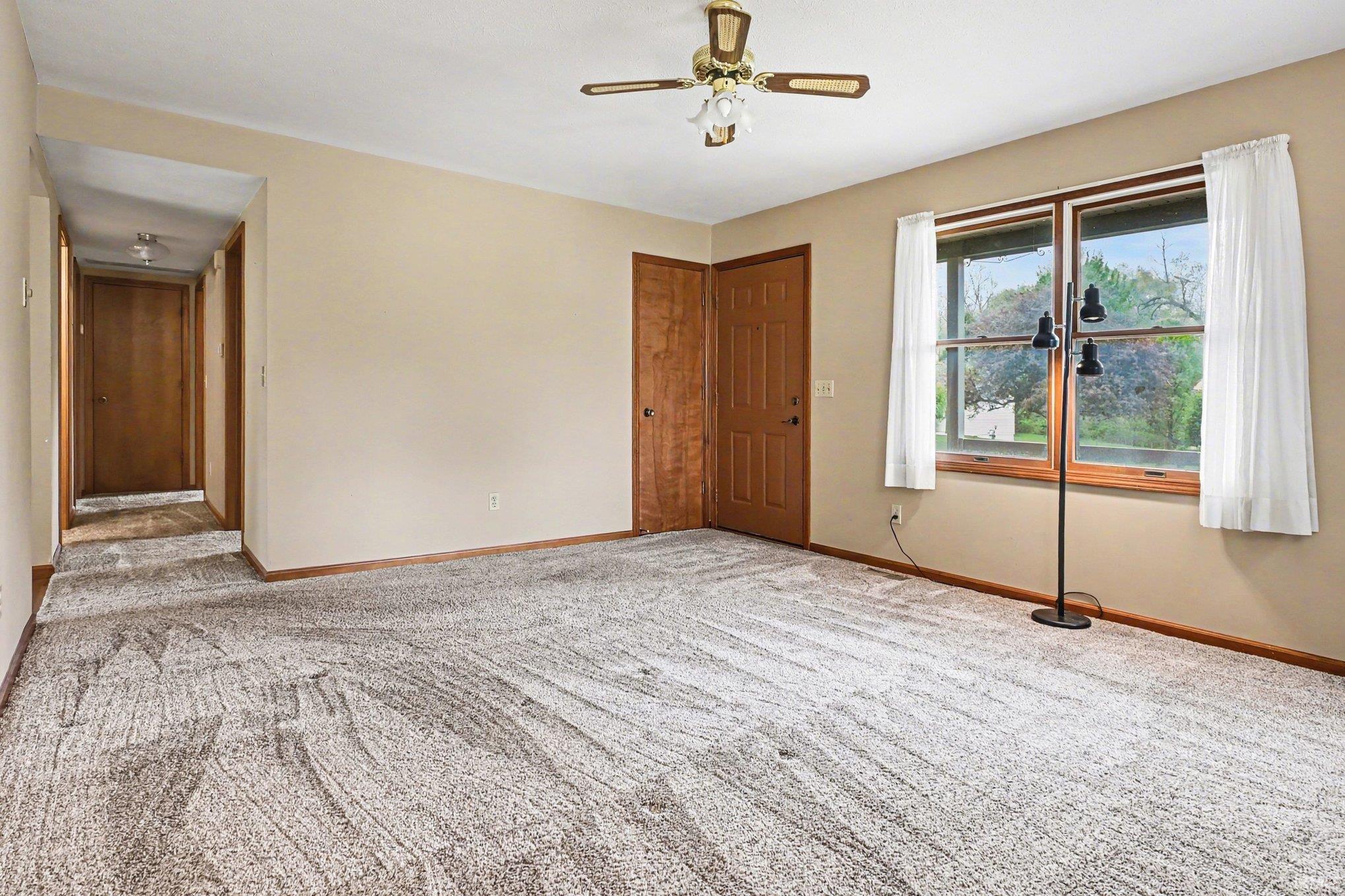 Carpeted room with a ceiling fan, two windows, two paneled doors, and a hallway entrance