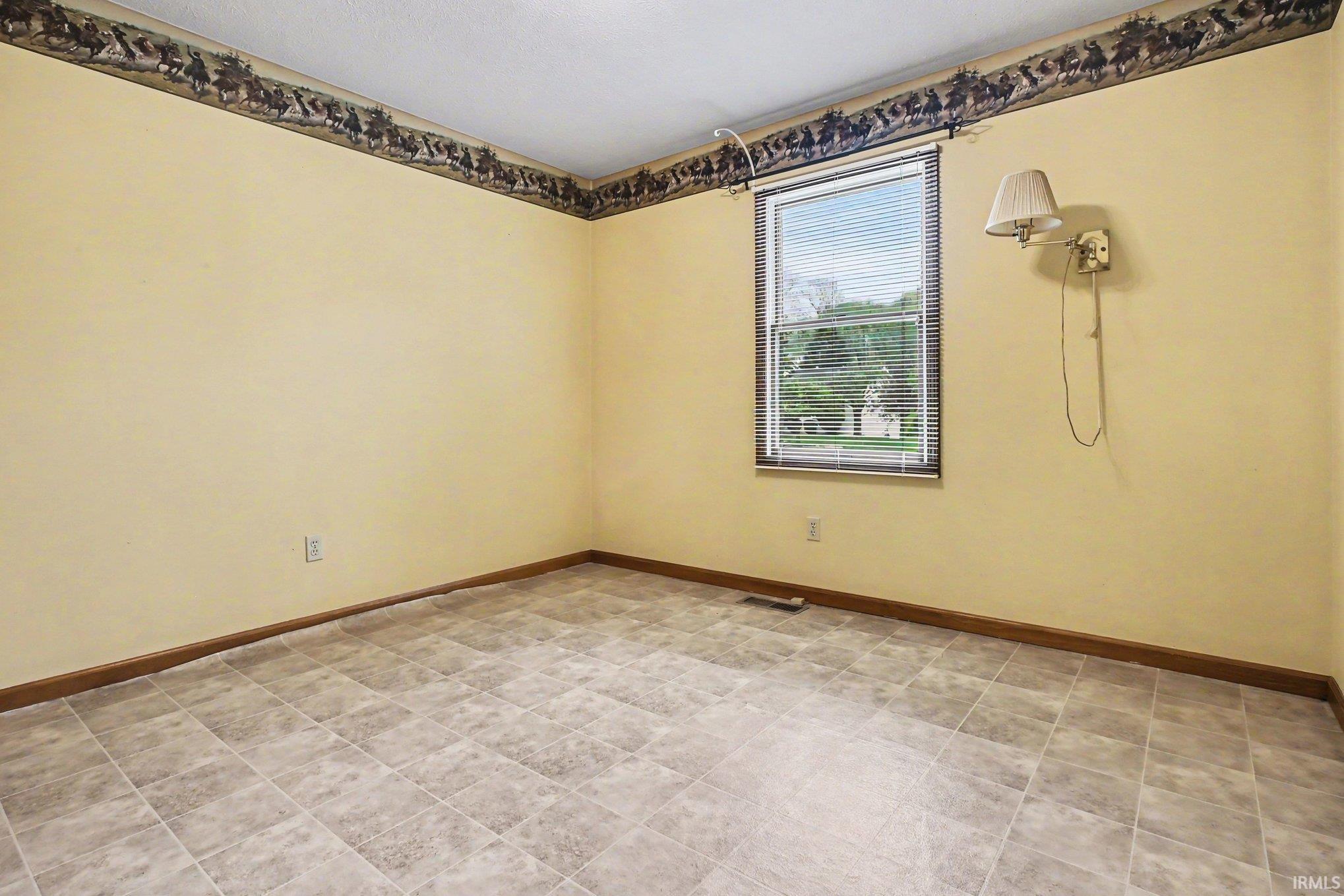 Room featuring tiled flooring, a single window with blinds, and light-toned walls with a decorative border