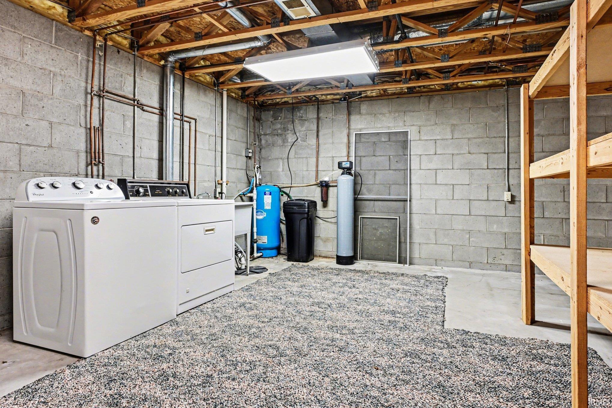 Utility area featuring exposed wood ceiling joists, concrete block walls, and concrete flooring