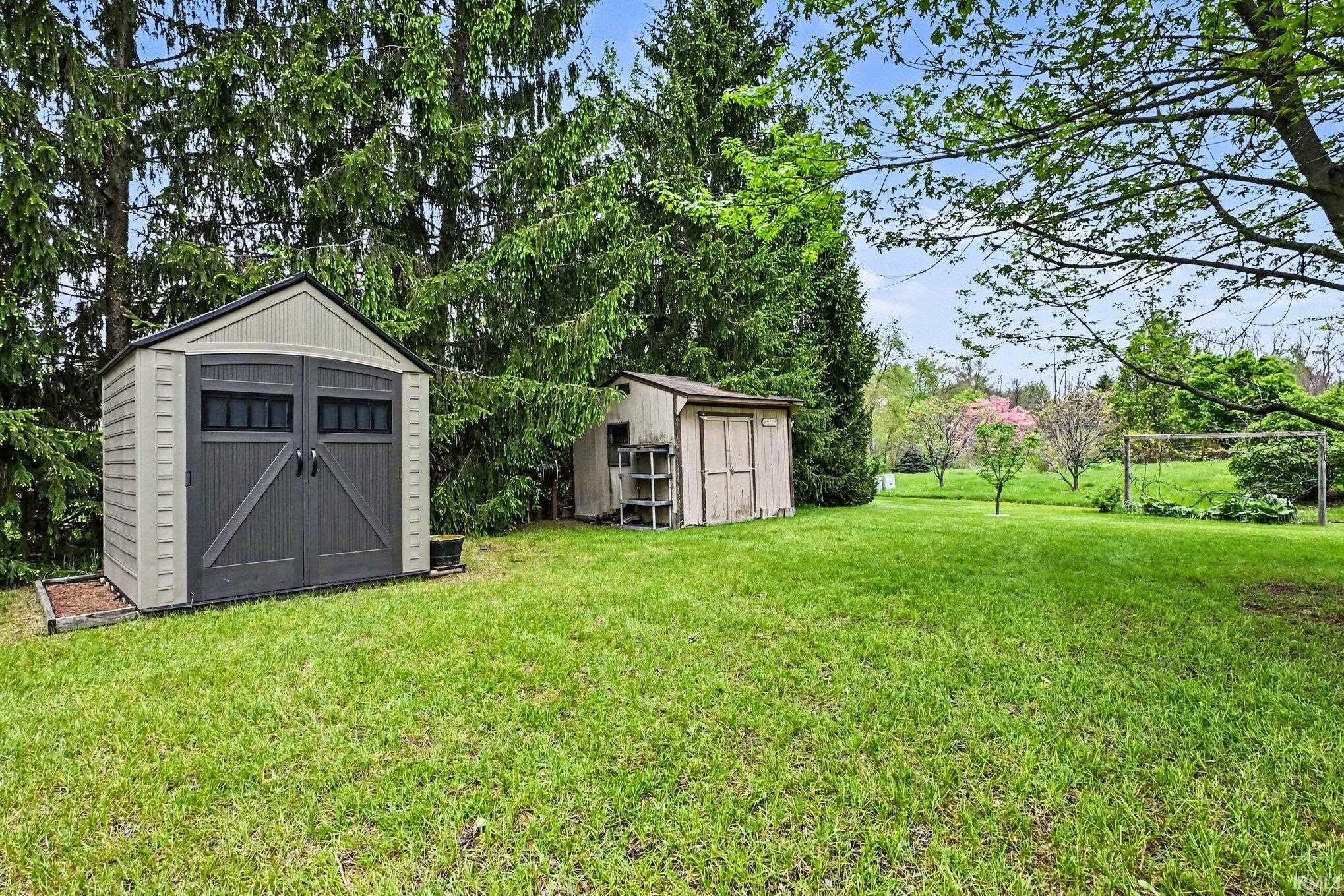 Expansive green lawn featuring two exterior storage sheds, mature trees, and landscaping