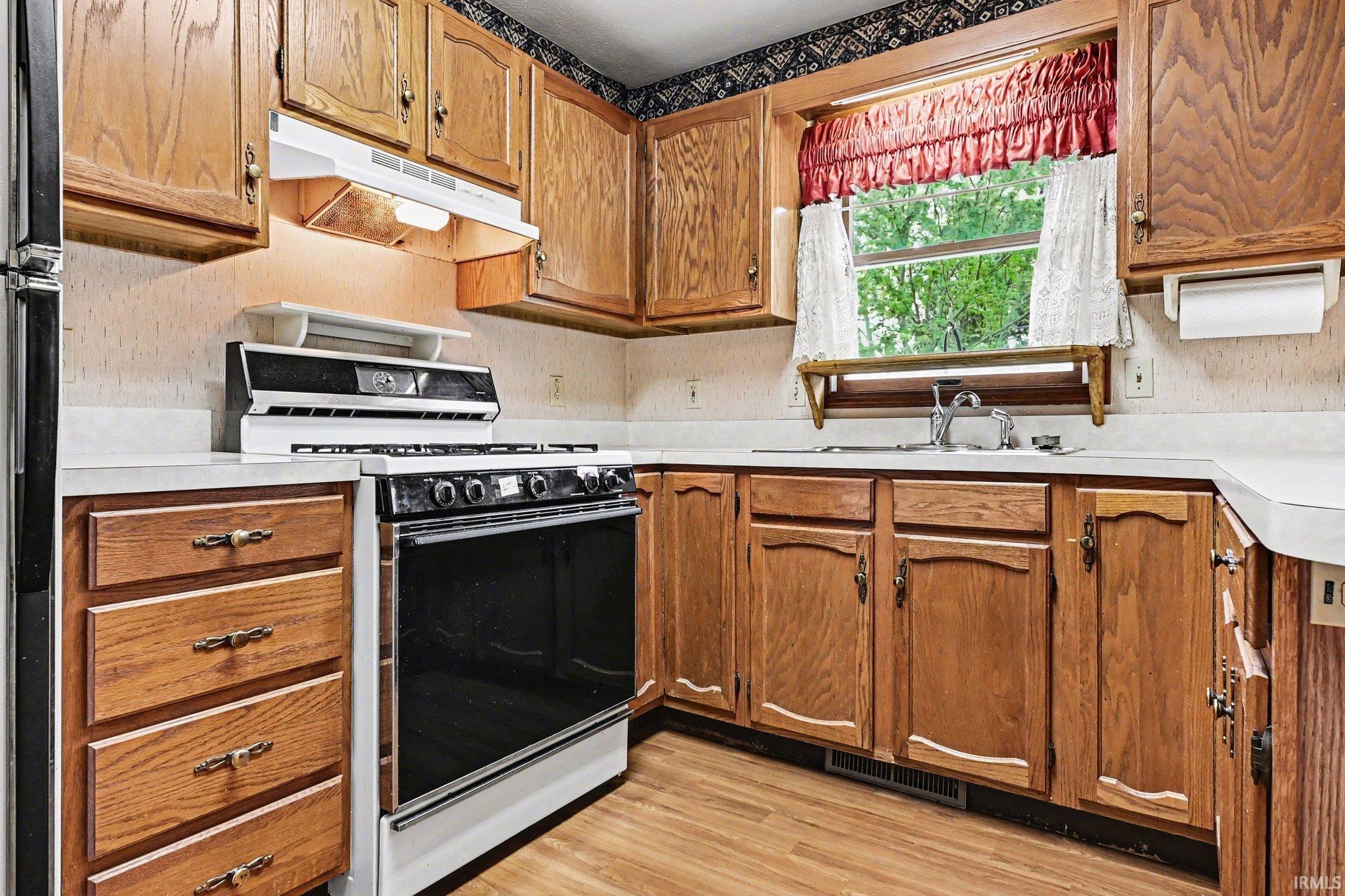 Kitchen featuring wood cabinetry with brass hardware, white countertops, and wood-finish flooring
