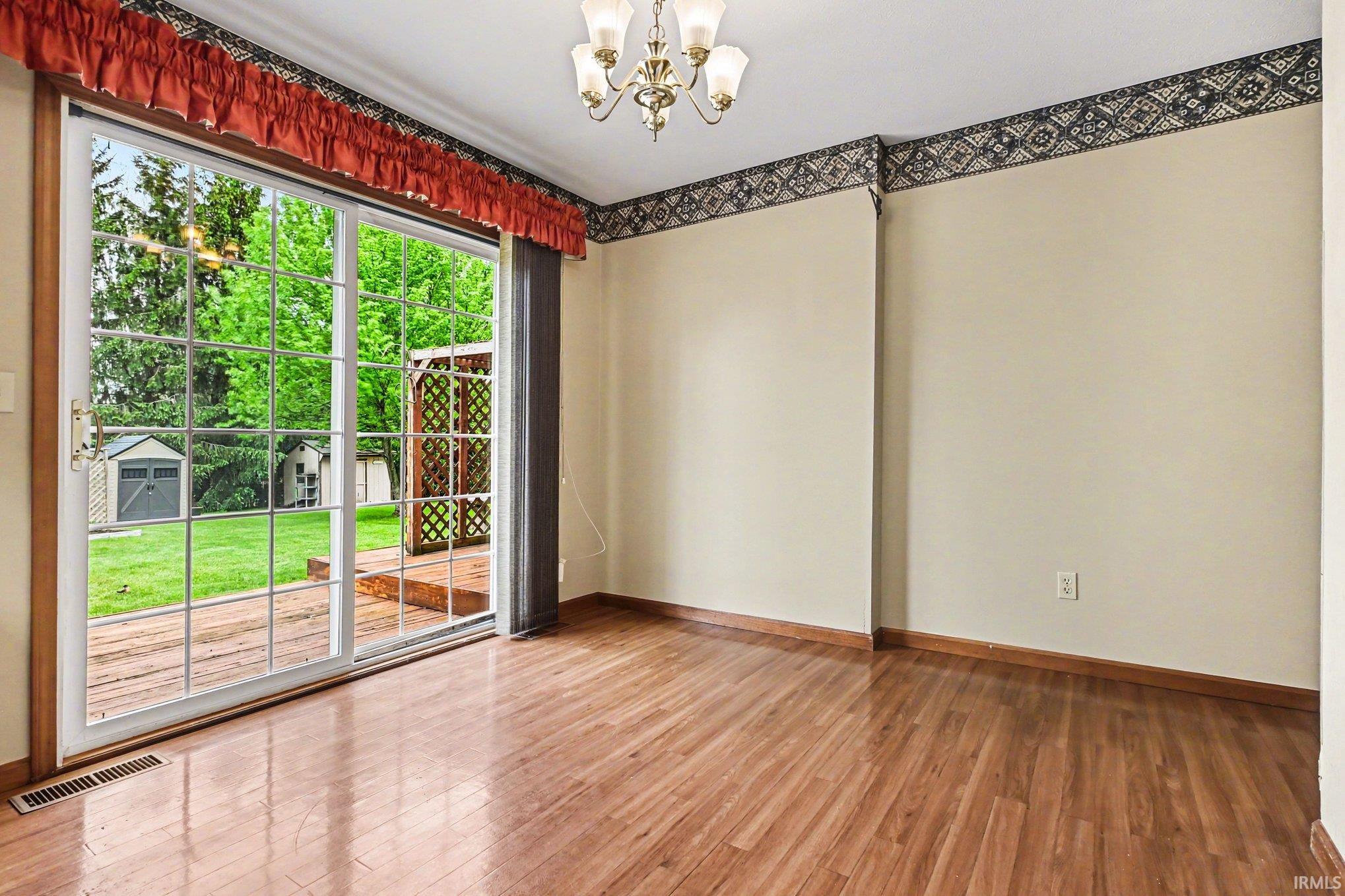Hardwood-finish flooring throughout, featuring sliding glass doors providing access to an exterior deck and a green backyard with mature trees