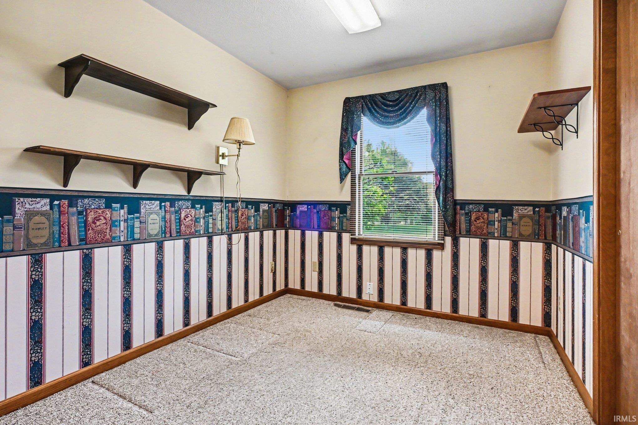Room featuring a window with blinds, sconce lighting, and wall-mounted shelving