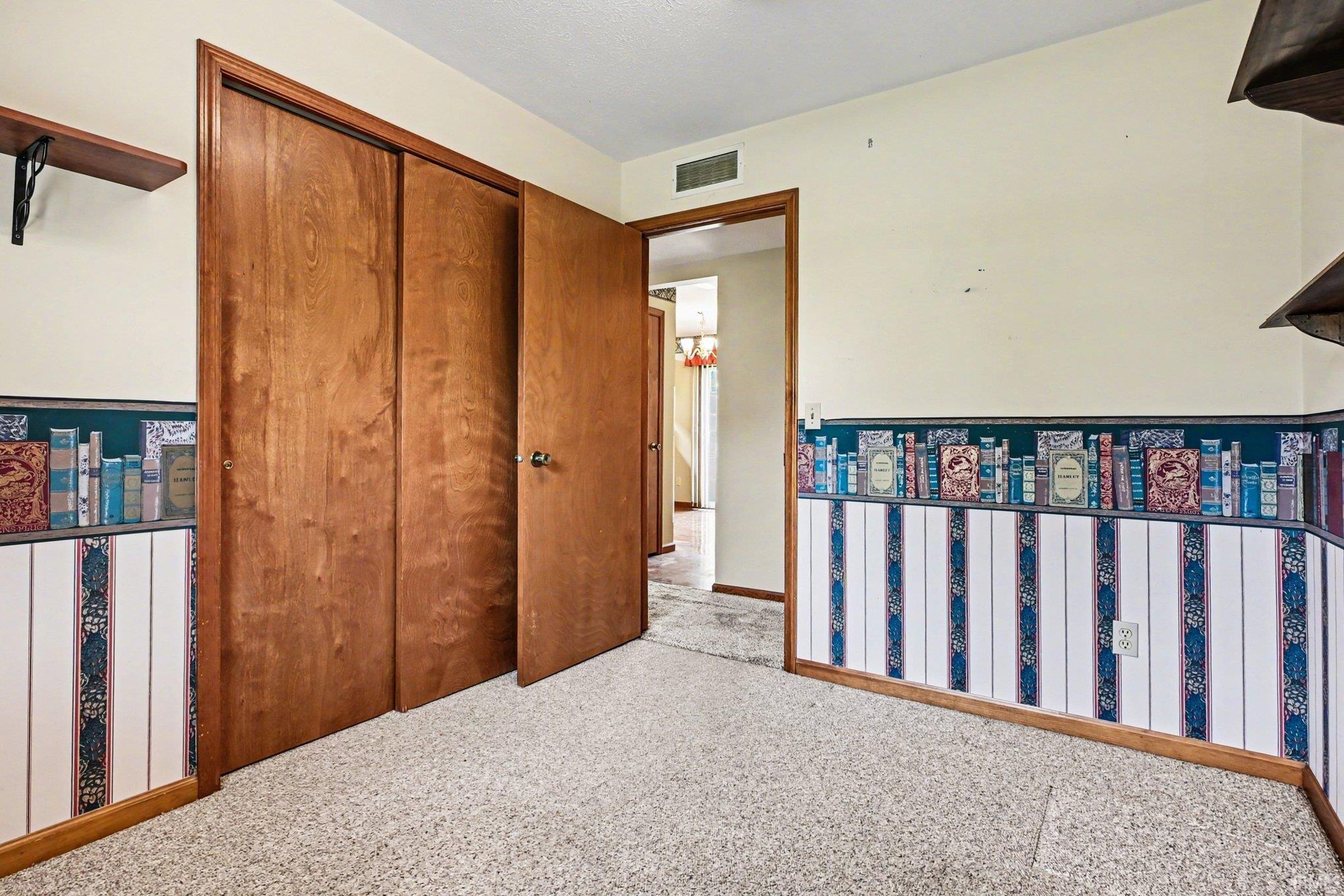 Room featuring light-colored wall paint with decorative wallpaper, wood-finish closet doors, and carpet flooring
