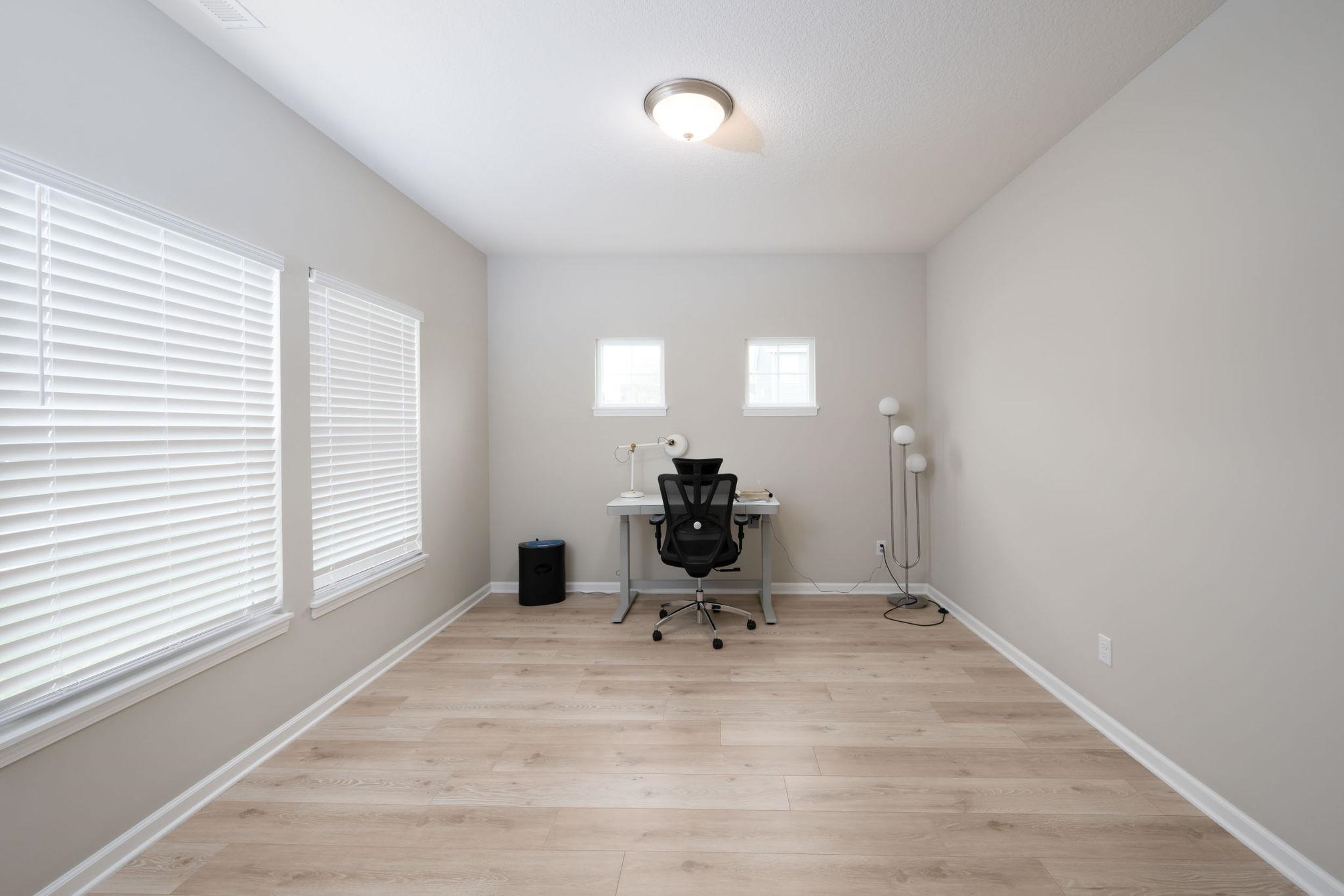 Bright interior space featuring wood-finish flooring, two large windows with blinds, two smaller windows, and a ceiling-mounted light fixture