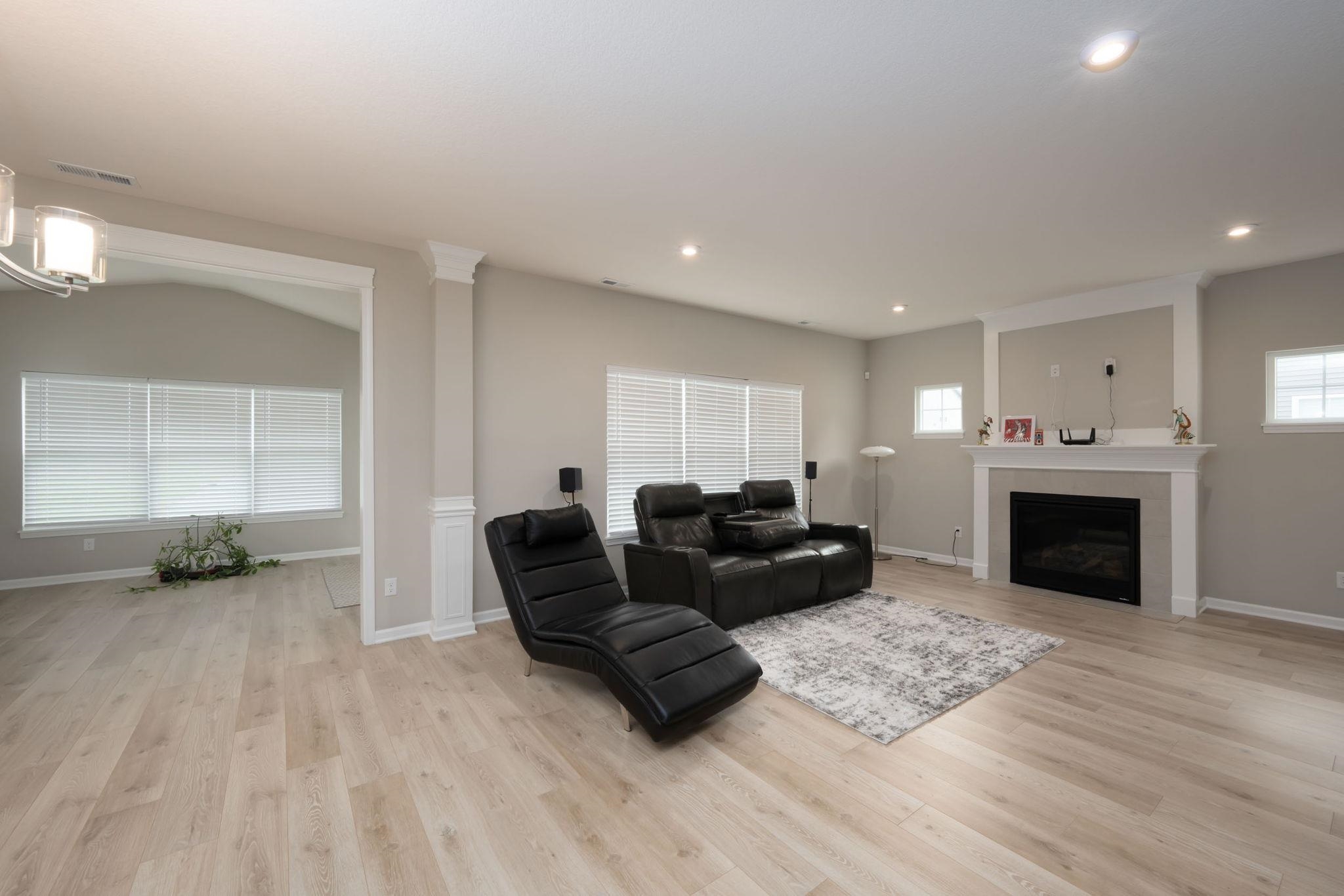 Spacious living area featuring wood-finish flooring, a fireplace with a white mantel, recessed lighting, and an arched entryway with decorative trim