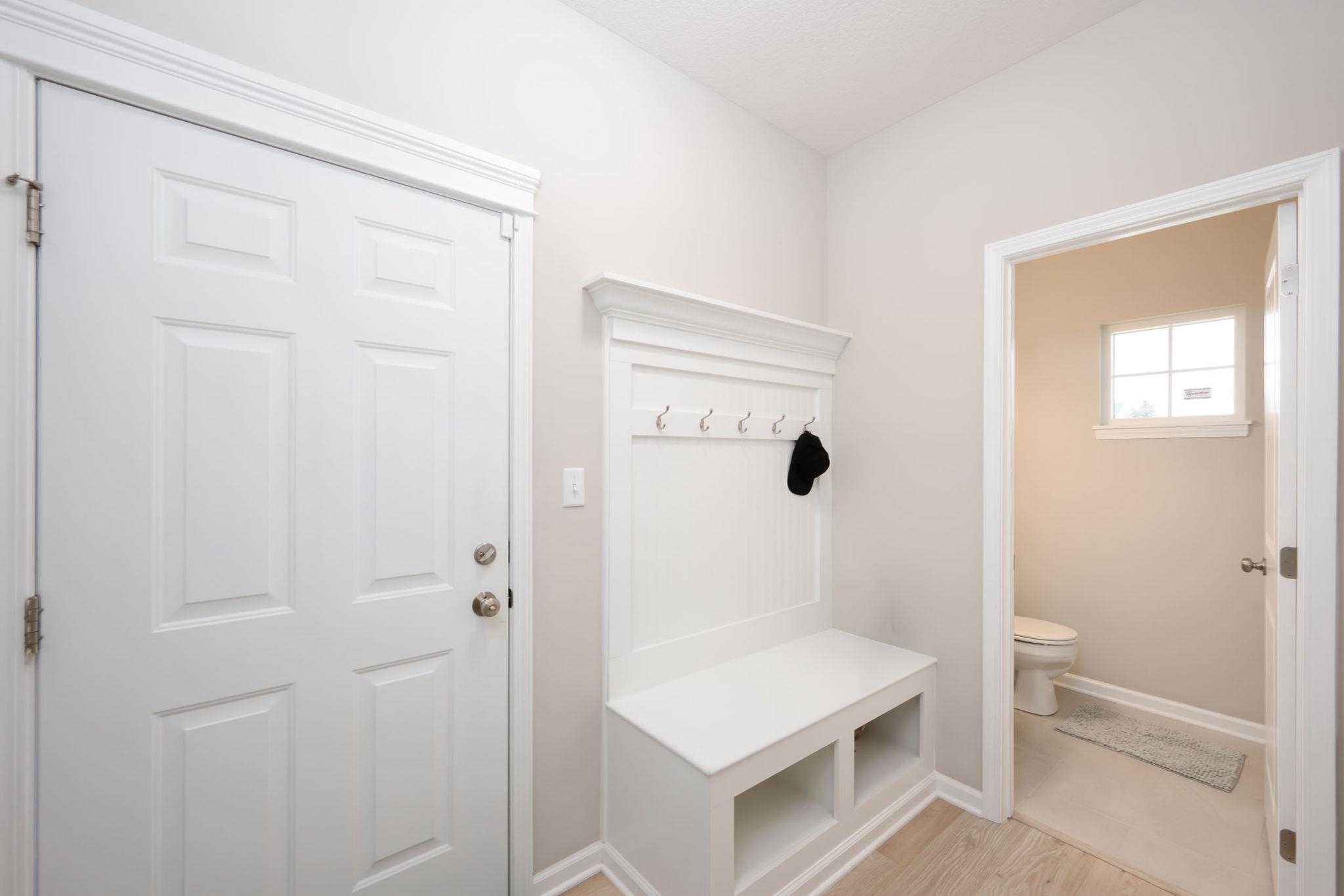 Entryway featuring a white paneled door, built-in mudroom bench with storage cubbies and coat hooks, and wood-finish flooring