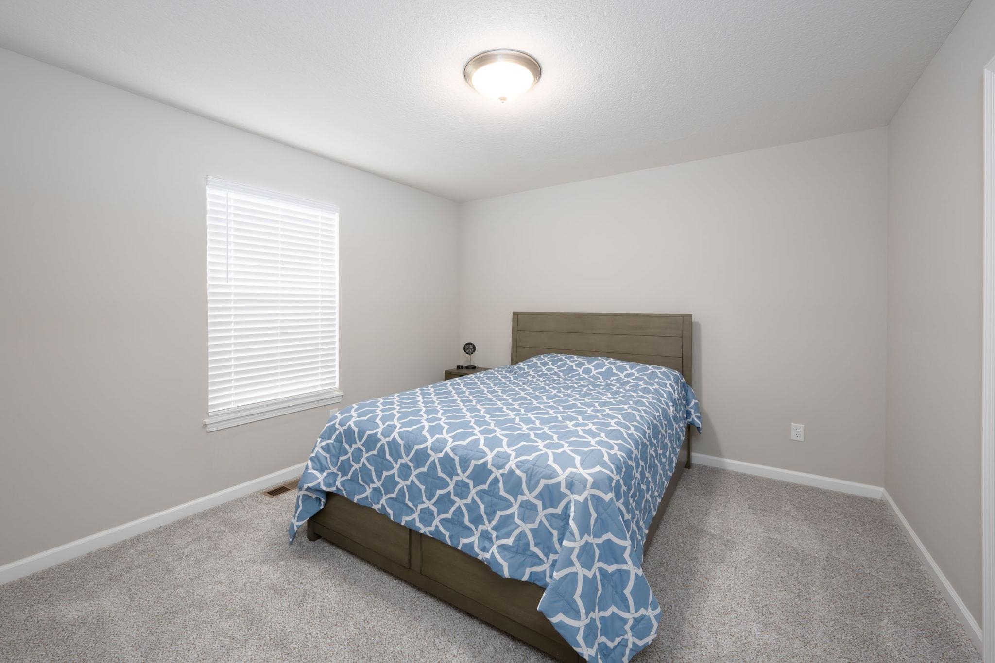 Neutral-toned room featuring a single window with blinds, light gray wall paint, and gray carpeted flooring