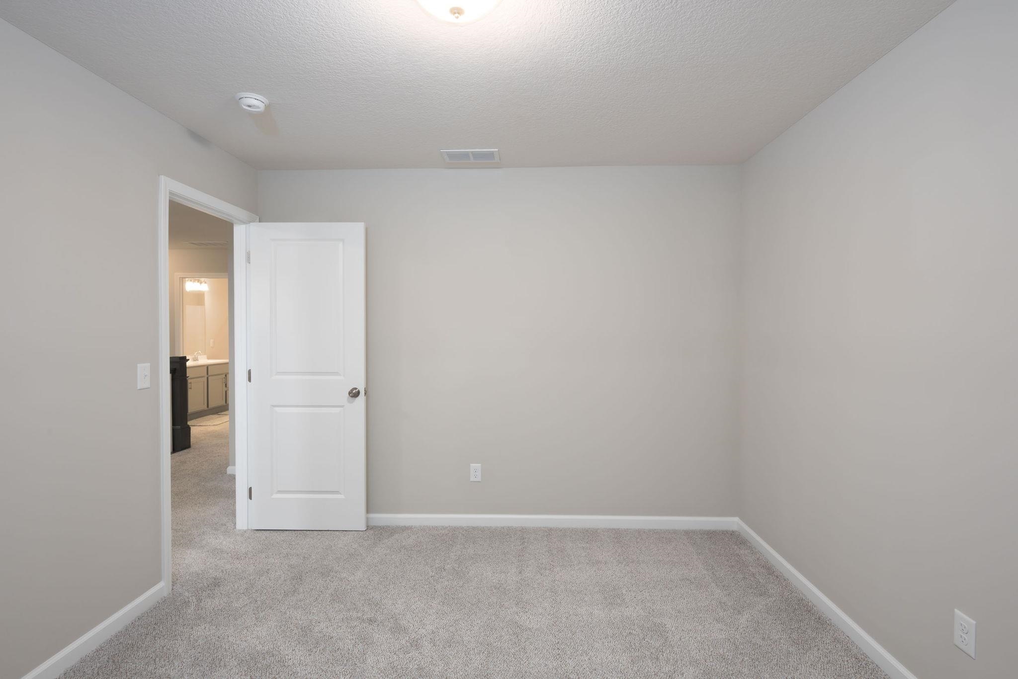 Light gray wall finishes with white trim, gray carpeted flooring, and a white interior door