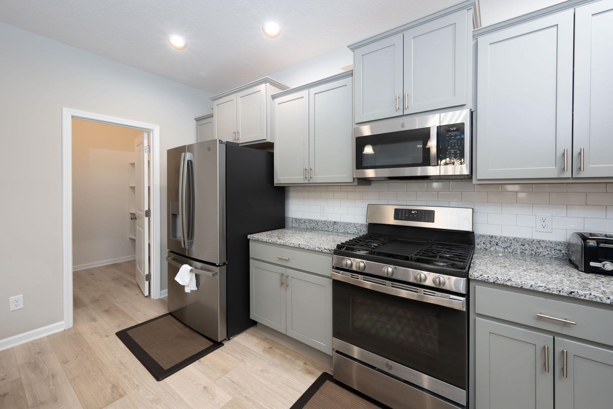 Kitchen featuring light wood-finish flooring, stainless steel appliances, grey cabinetry, and white subway tile backsplash