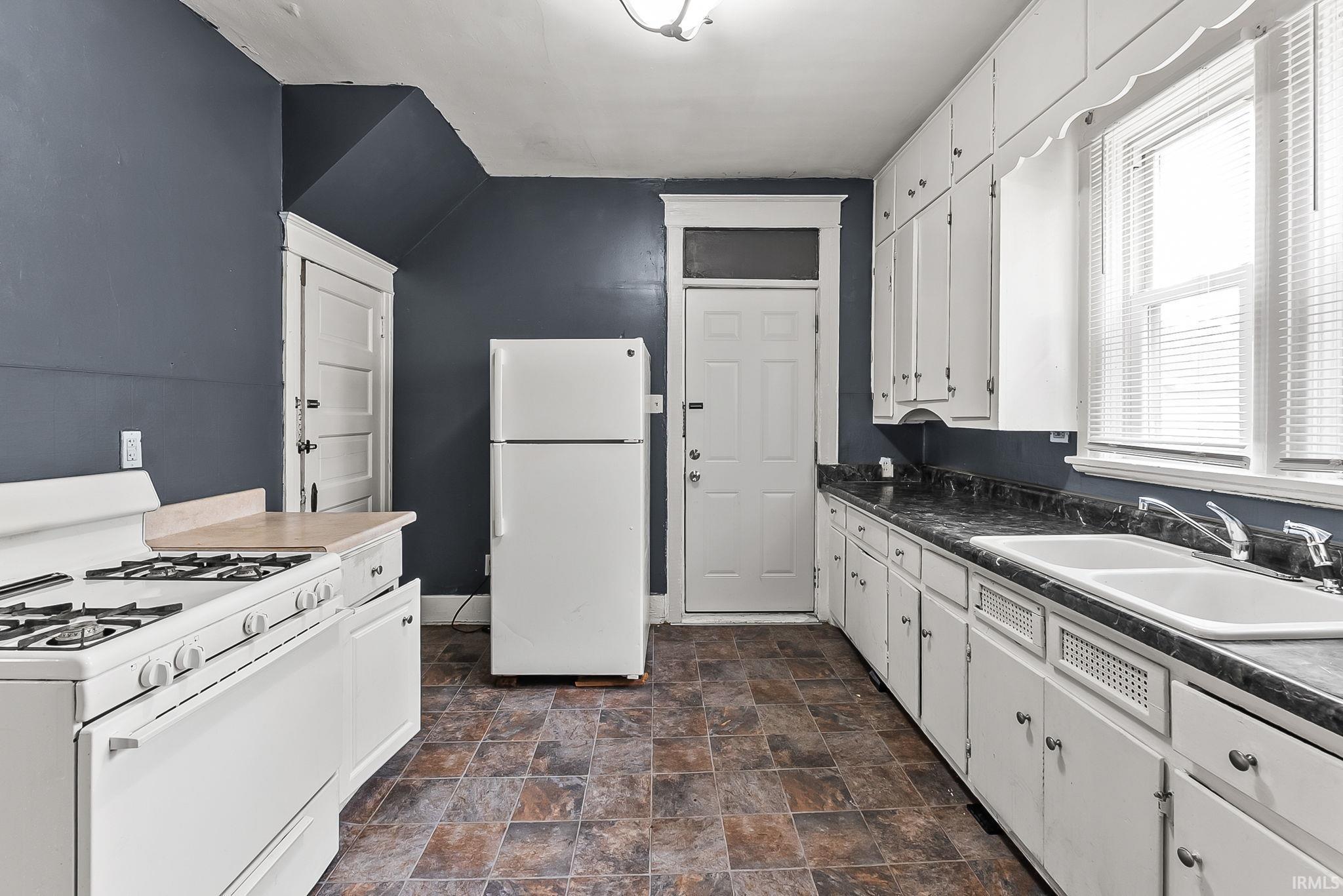 Kitchen featuring white cabinetry, a gas range, a dual-basin sink, and dark countertops