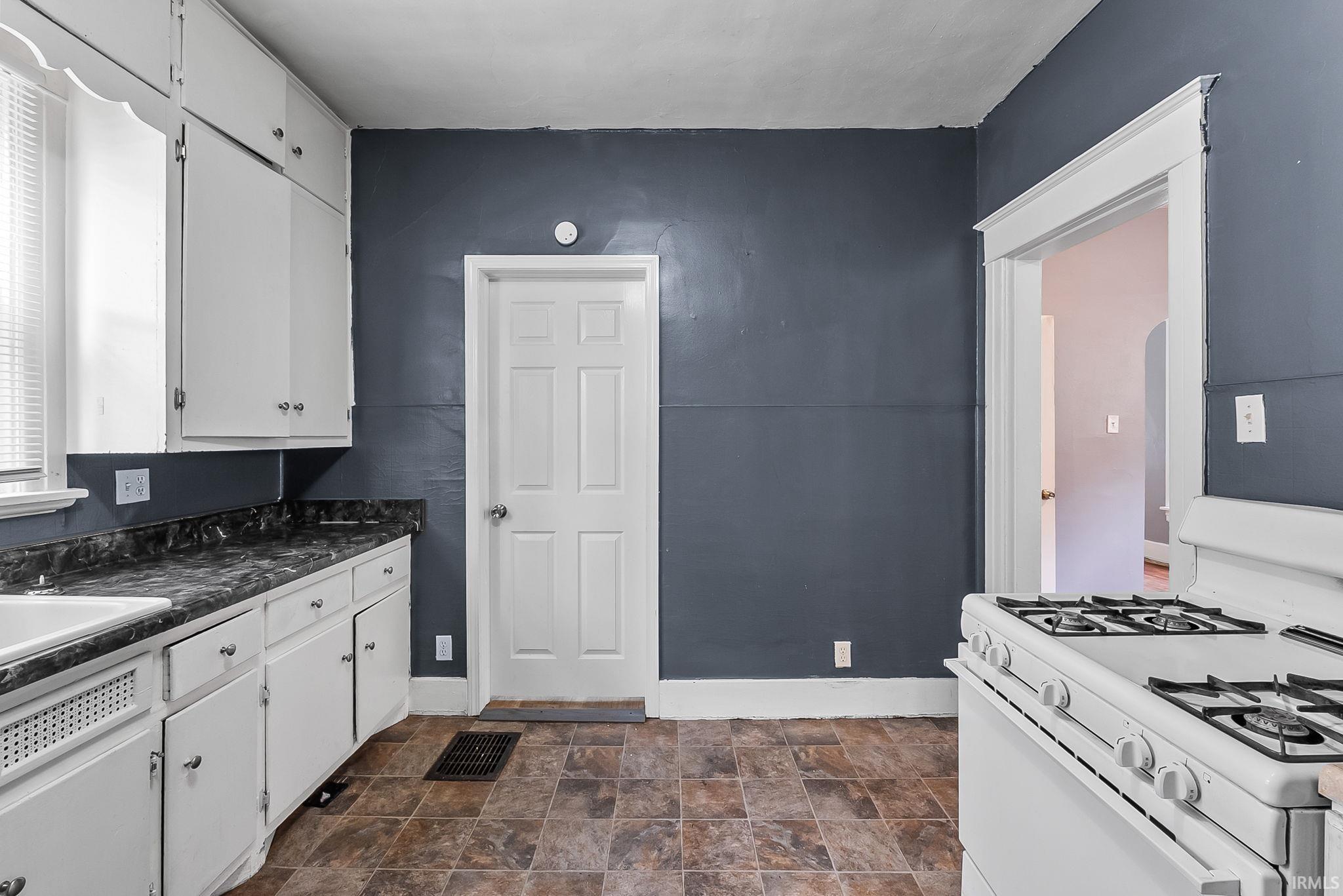 Kitchen featuring a built-in white gas range, white cabinetry, dark speckled countertops, and tile flooring