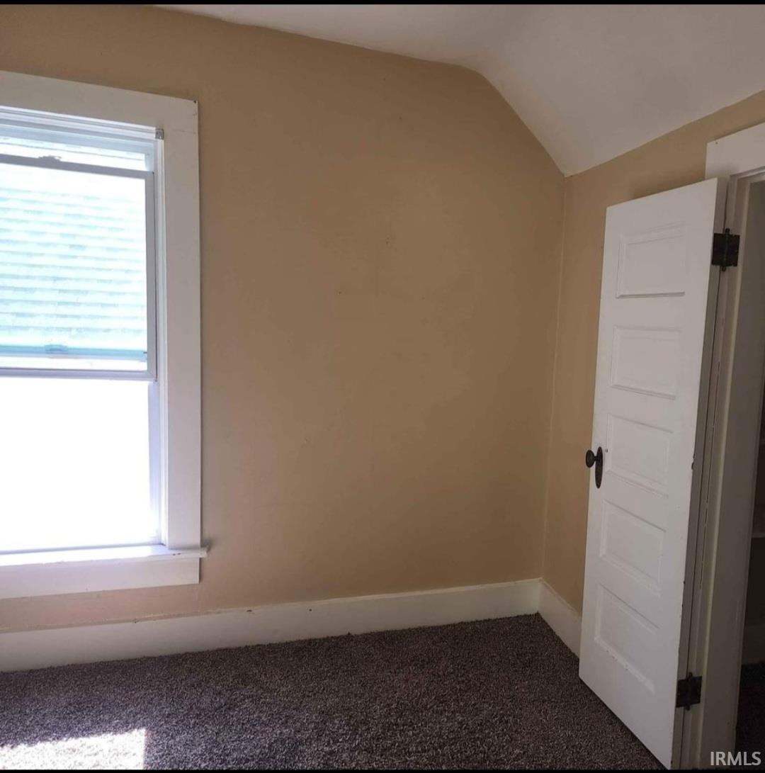 Room featuring a single-pane window with white trim, tan painted walls, and dark speckled carpeting