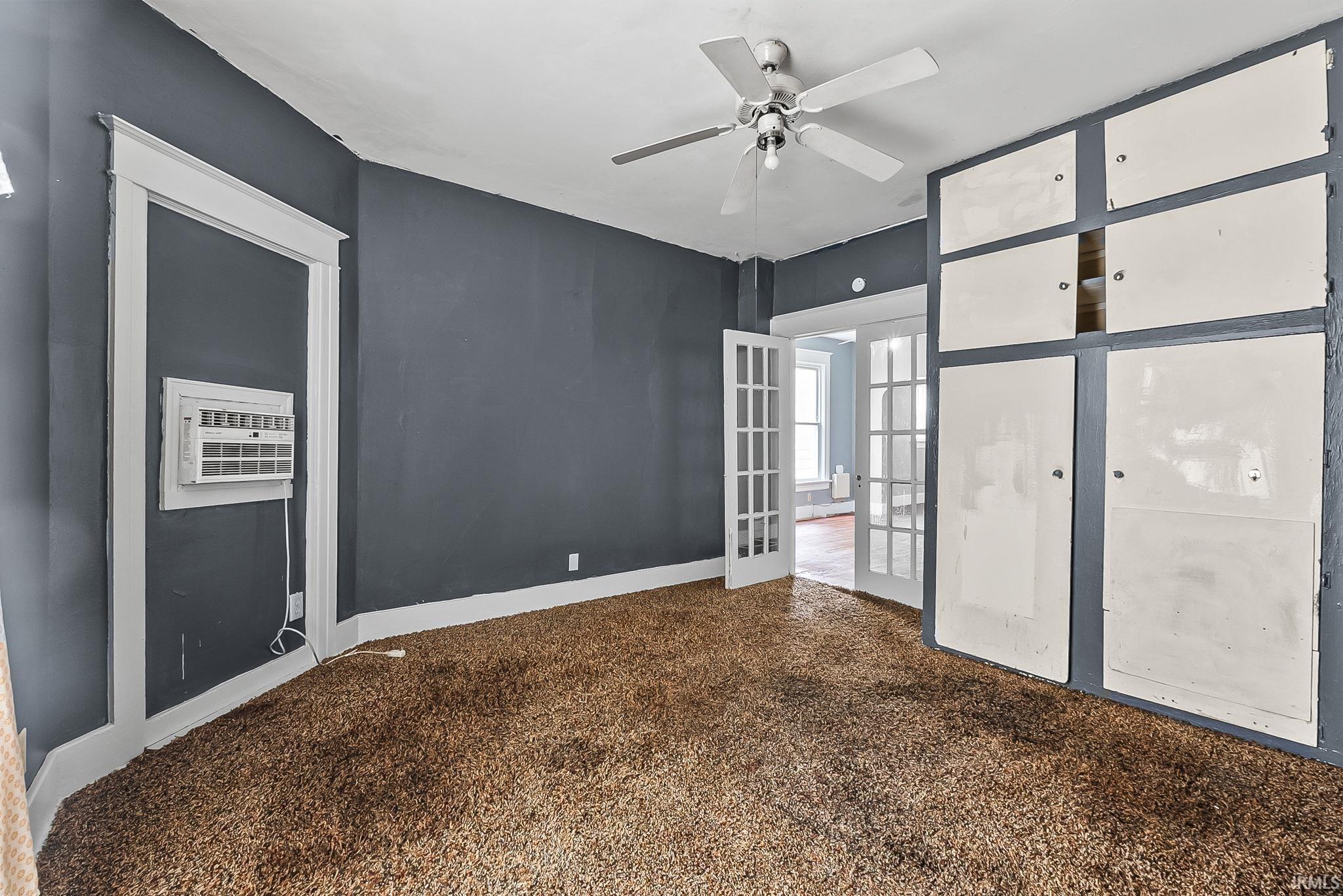 Carpeted room featuring a ceiling fan, built-in wall cabinetry, and French doors