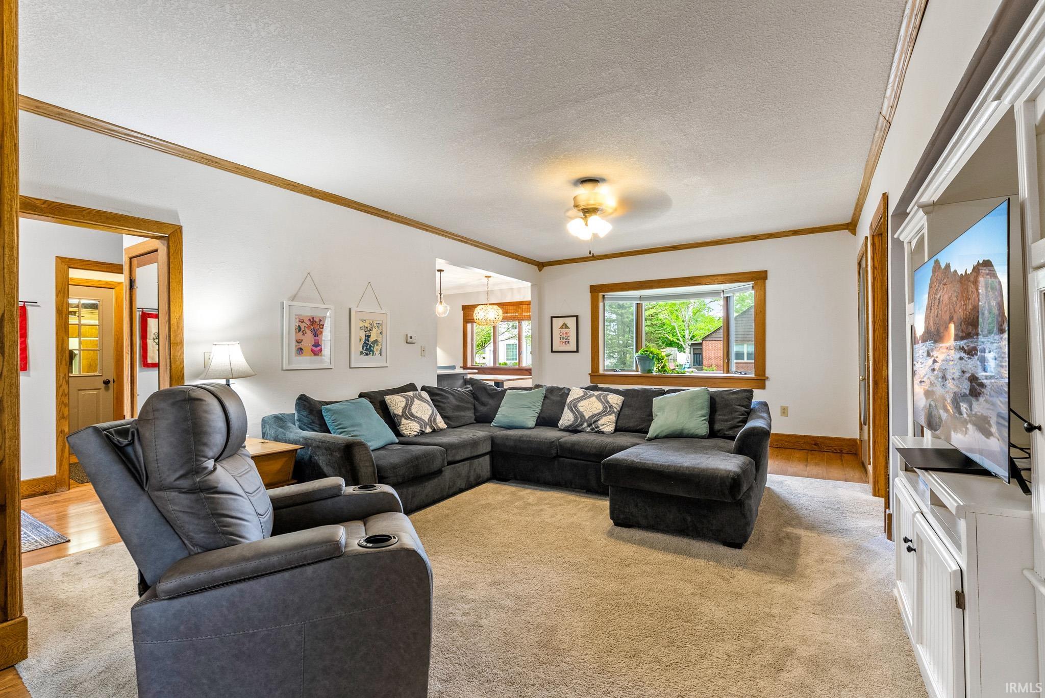 Spacious living area featuring light-colored carpeting, white walls with natural wood trim, and a built-in media cabinet