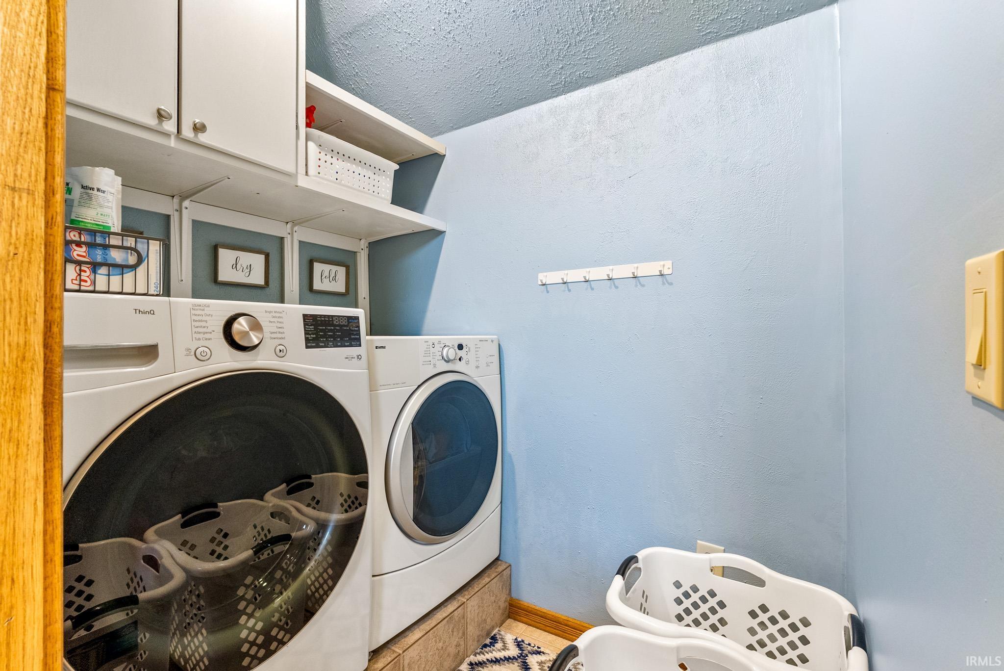 Dedicated laundry area featuring white front-loading appliances, upper white cabinetry, and open shelving