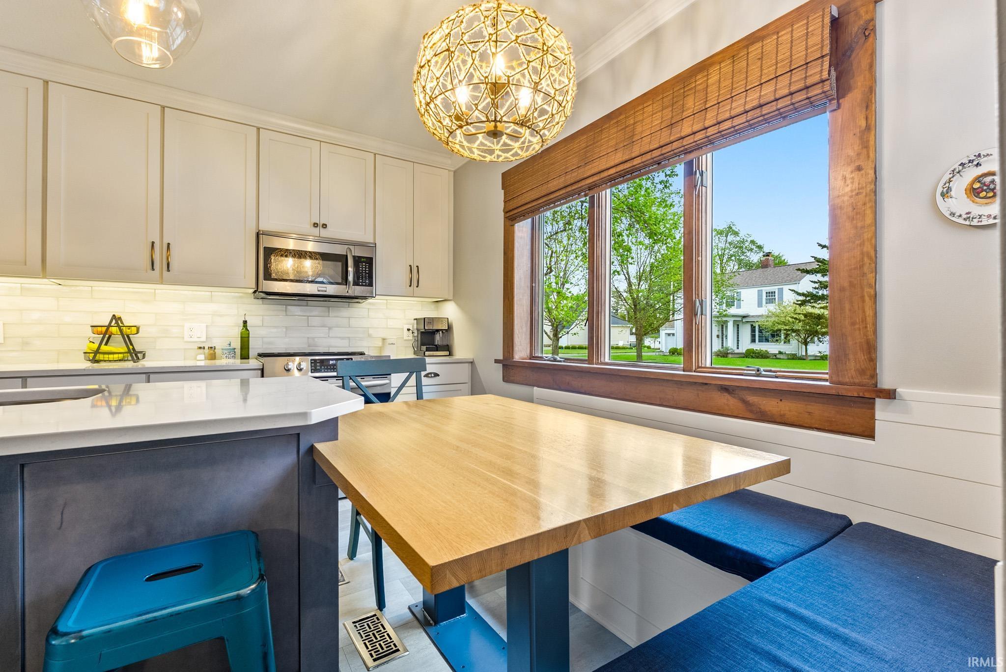 Integrated kitchen and dining area featuring a built-in banquette, a light wood-finish tabletop, and a large multi-pane window