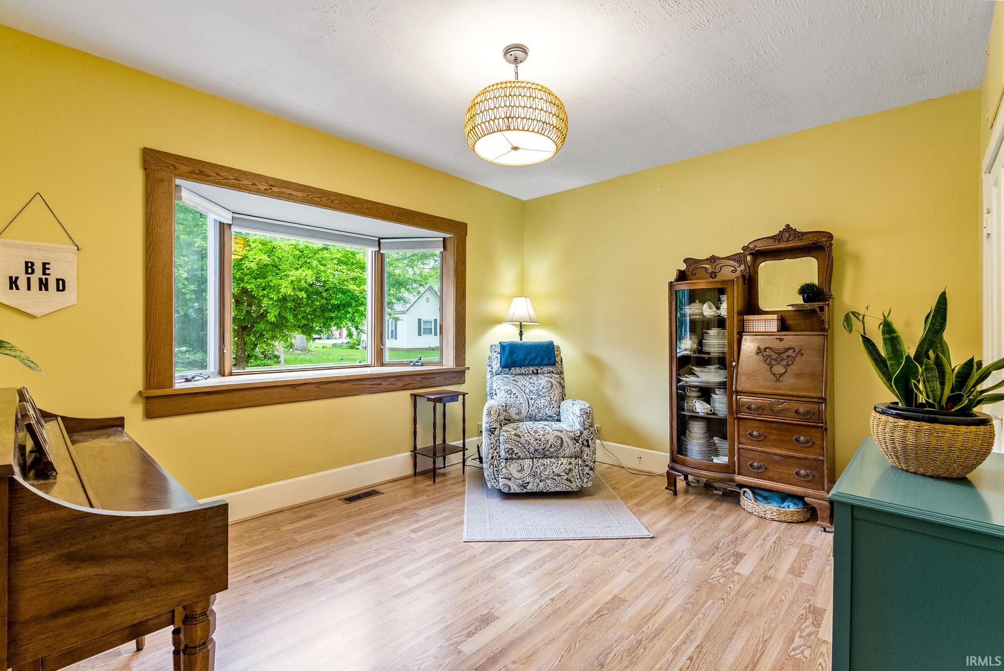 Spacious room featuring a prominent bay window with natural wood trim, wood-finish flooring, a textured ceiling, and a modern woven pendant light fixture