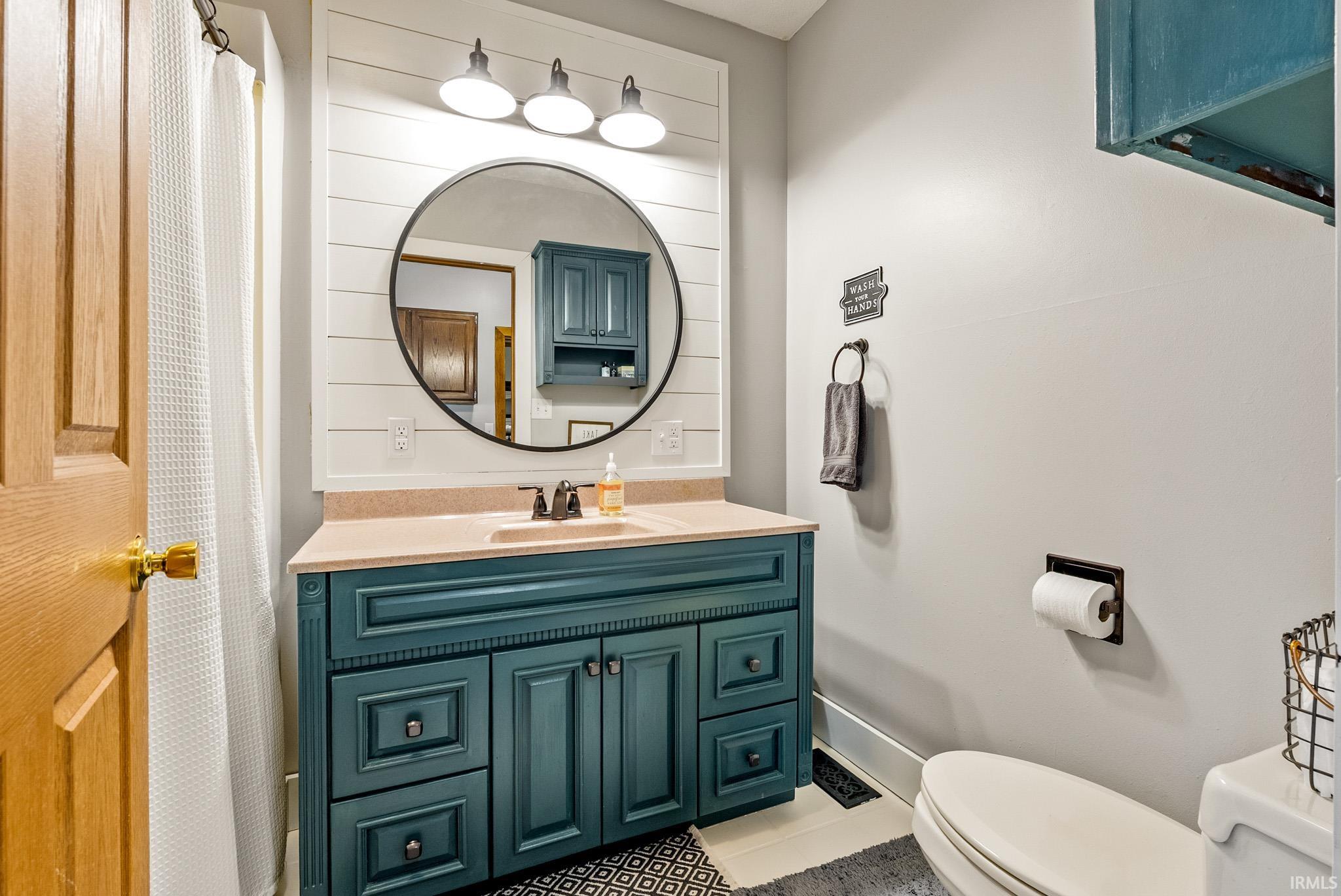 Bathroom vanity featuring a teal cabinet base with drawers and doors, a light-colored countertop with an integrated sink, and a circular mirror