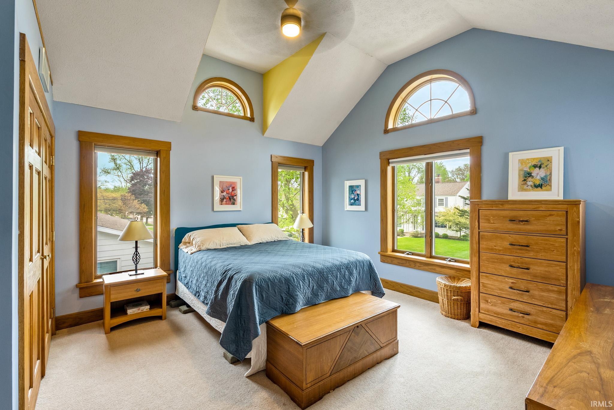 Vaulted ceiling room with multiple windows, wood-finish trim, and light-toned carpeting