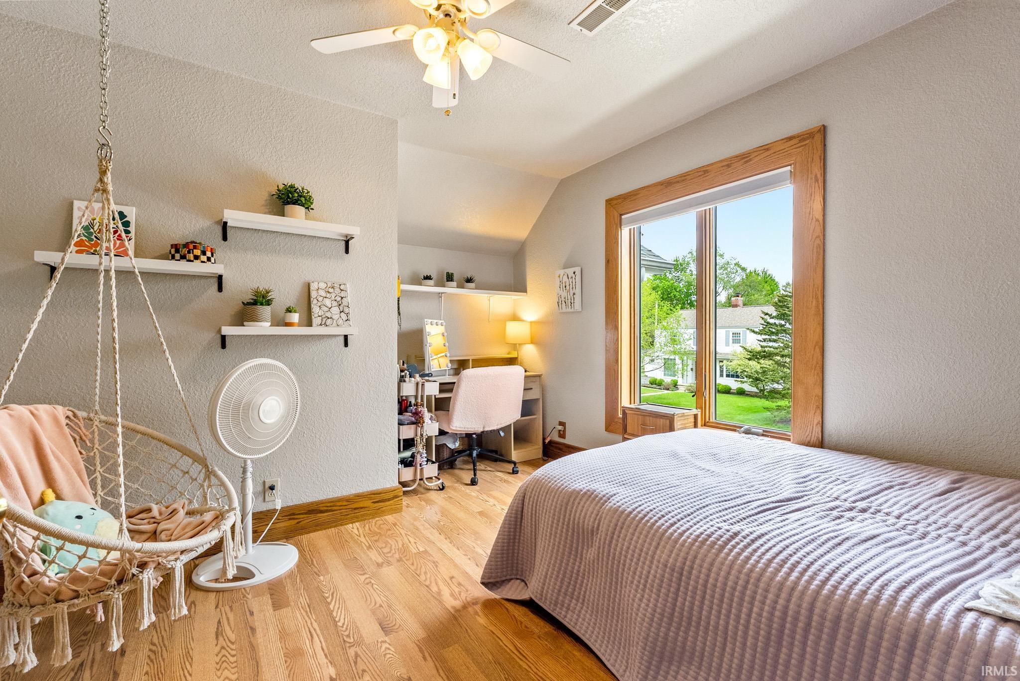 Hardwood flooring throughout, featuring a natural wood window frame, a ceiling fan with integrated lighting, and multiple wall-mounted shelves