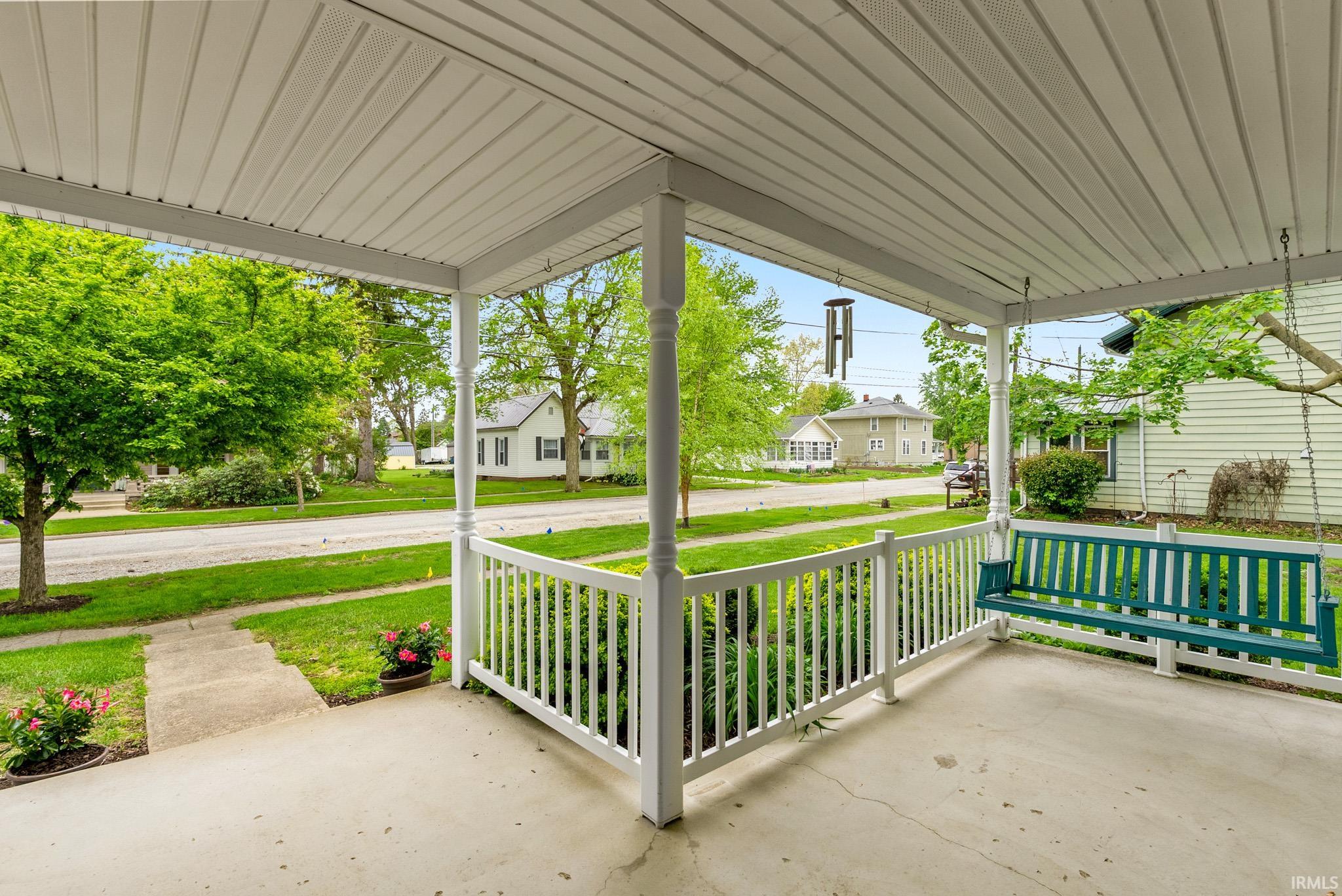 Covered front porch featuring a white railing and substantial support columns
