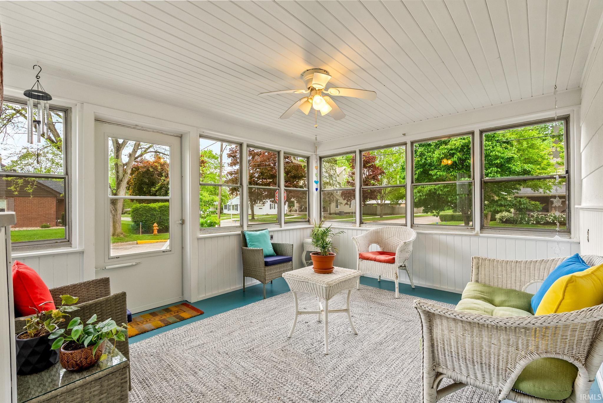 Bright sunroom featuring multiple windows, a paneled ceiling, painted wood-finish flooring, a ceiling fan, and an exterior door