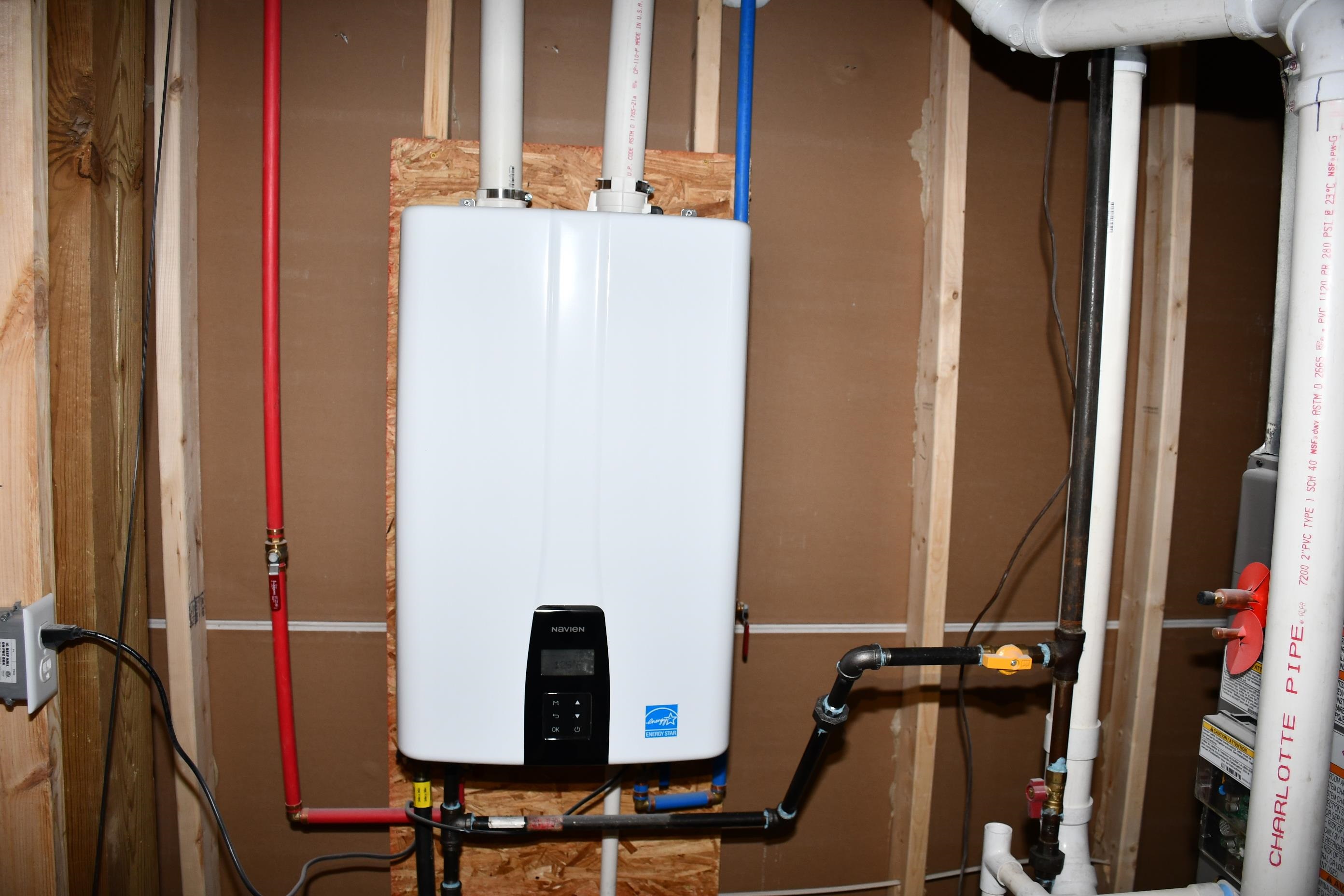 Tankless water heater installation with exposed wood framing and various utility lines