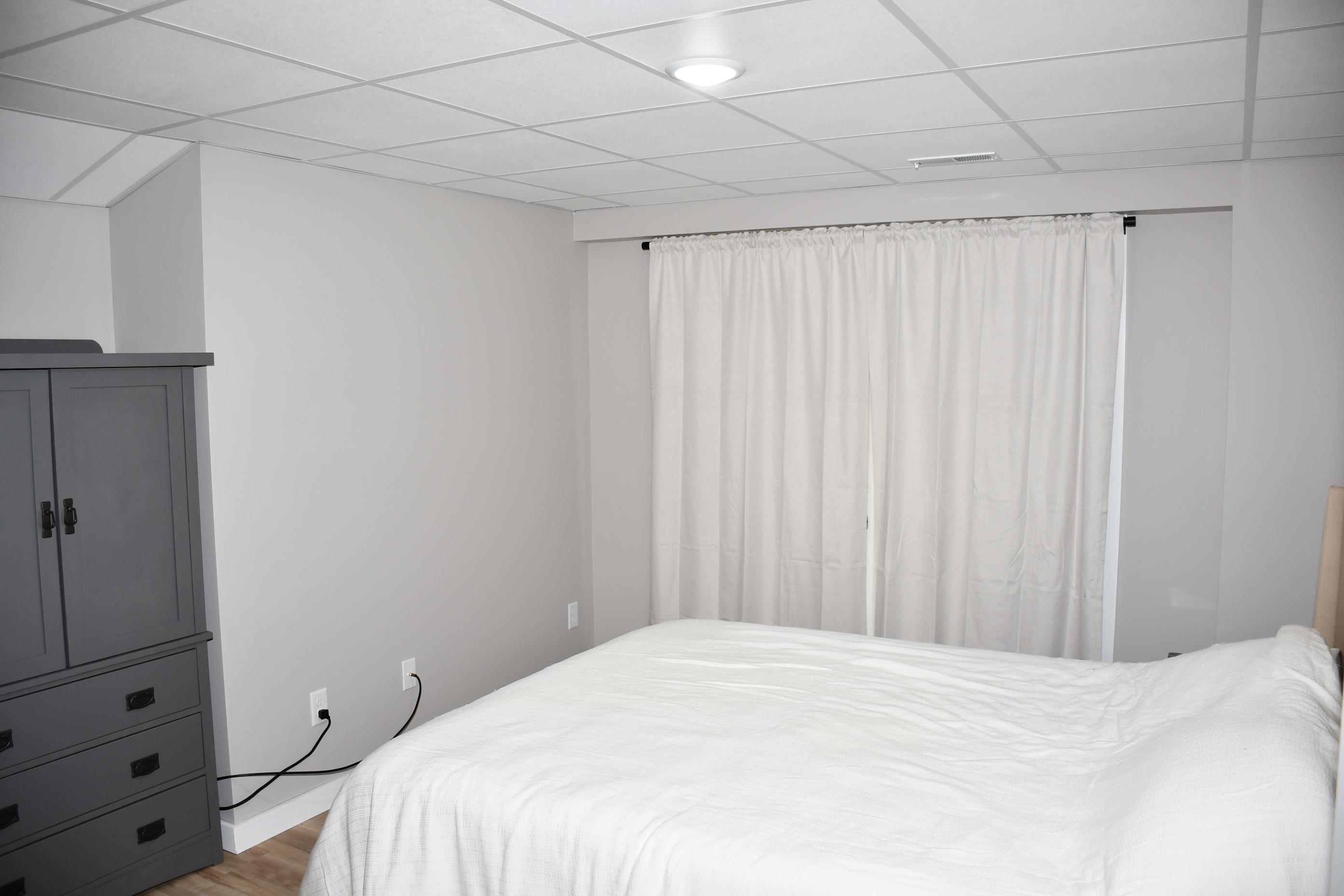 Bedroom featuring light neutral wall tones, drop ceiling with recessed lighting, and wood-finish flooring