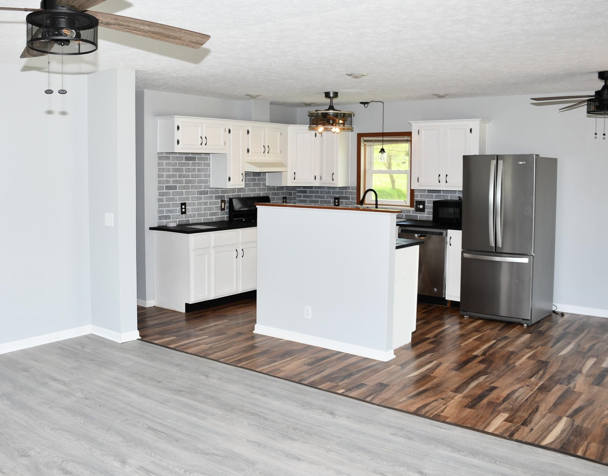 Open-concept kitchen featuring white cabinetry, dark countertops, and a gray subway tile backsplash