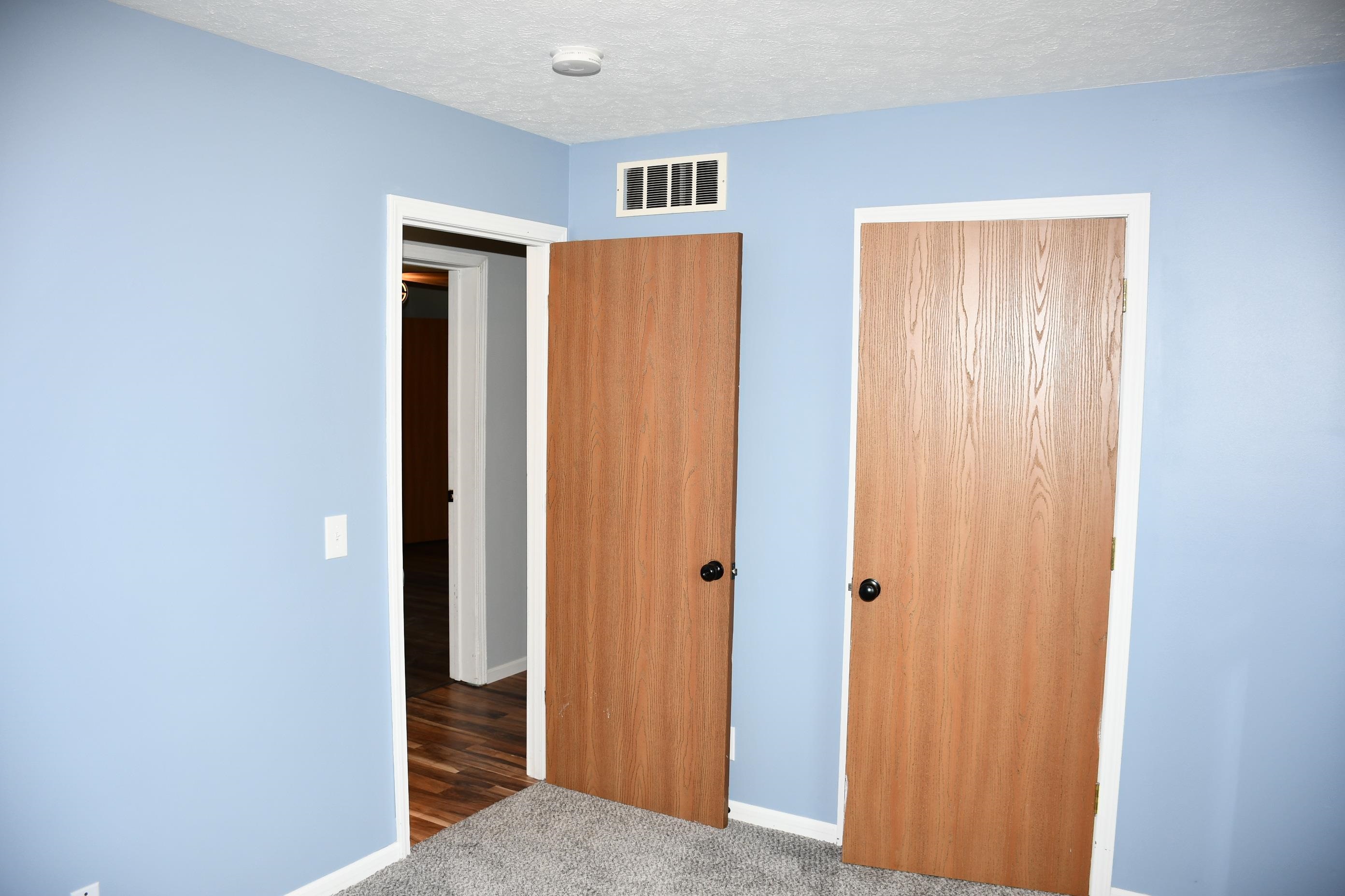 Bedroom featuring light blue painted walls, wood-finish interior doors with black hardware, white trim, and gray carpet flooring