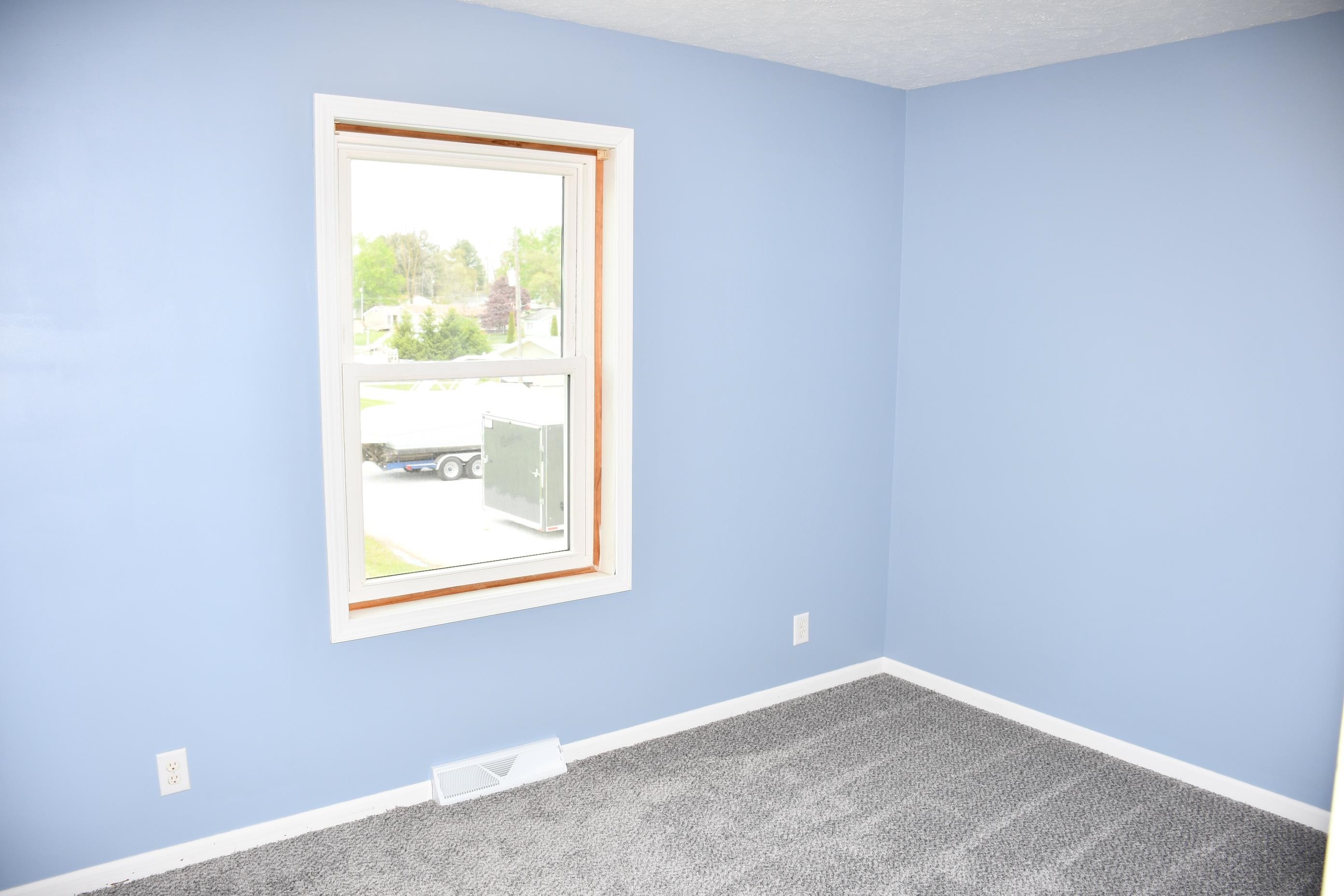 Bedroom featuring light blue walls, white trim, a single pane window, and grey carpet flooring