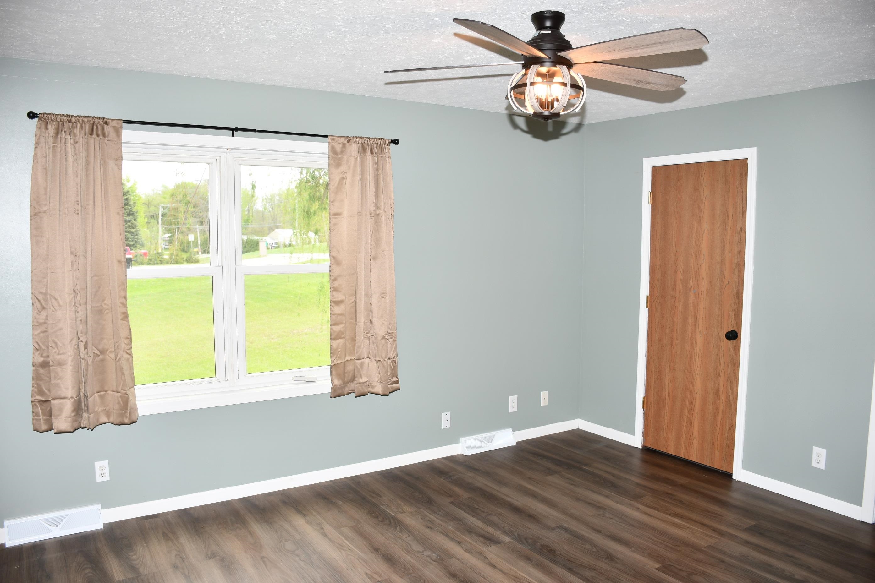 Room featuring a ceiling fan with integrated lighting, wood-finish flooring, and a large window