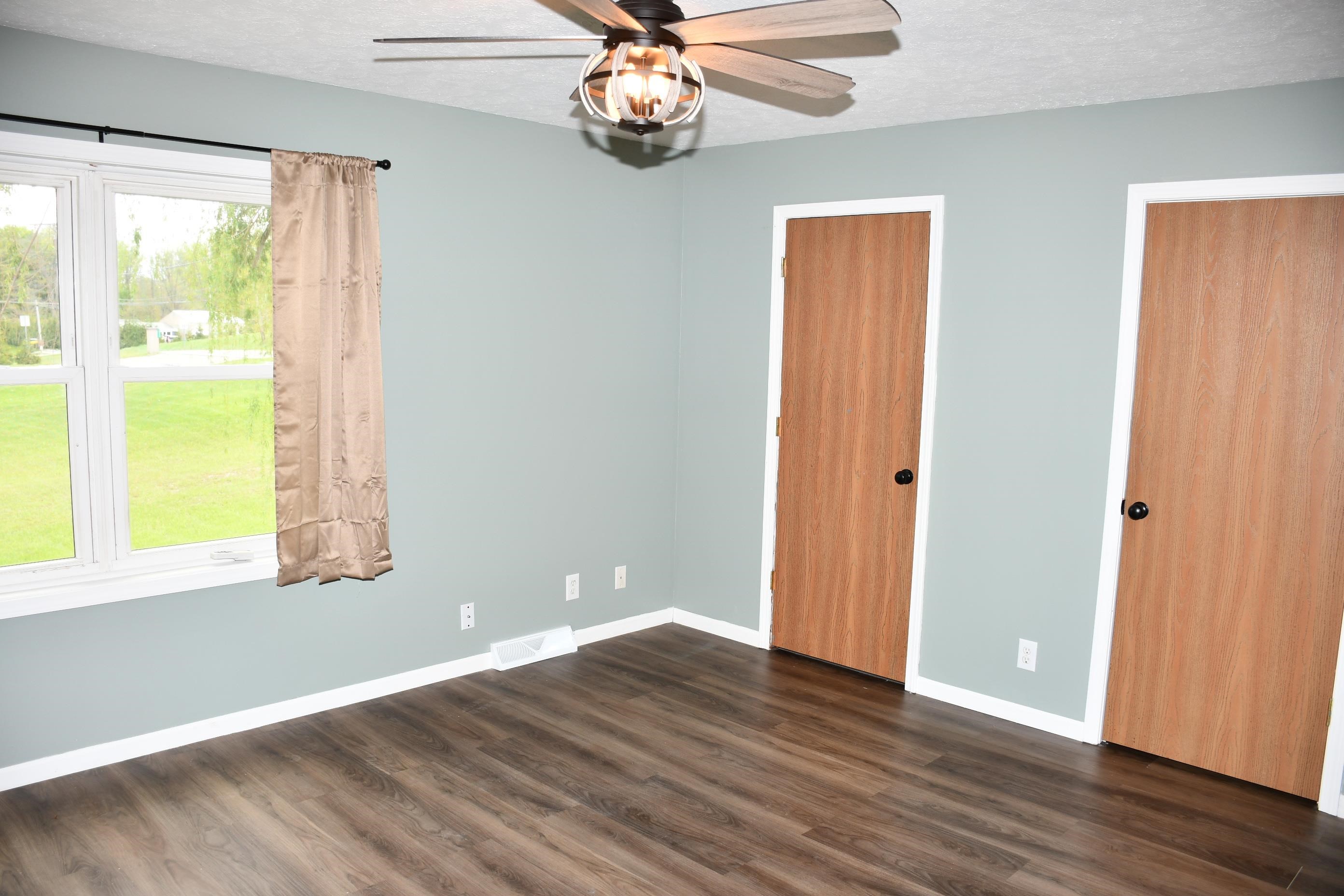 Spacious room featuring wood-finish flooring, light blue-grey walls, and white trim