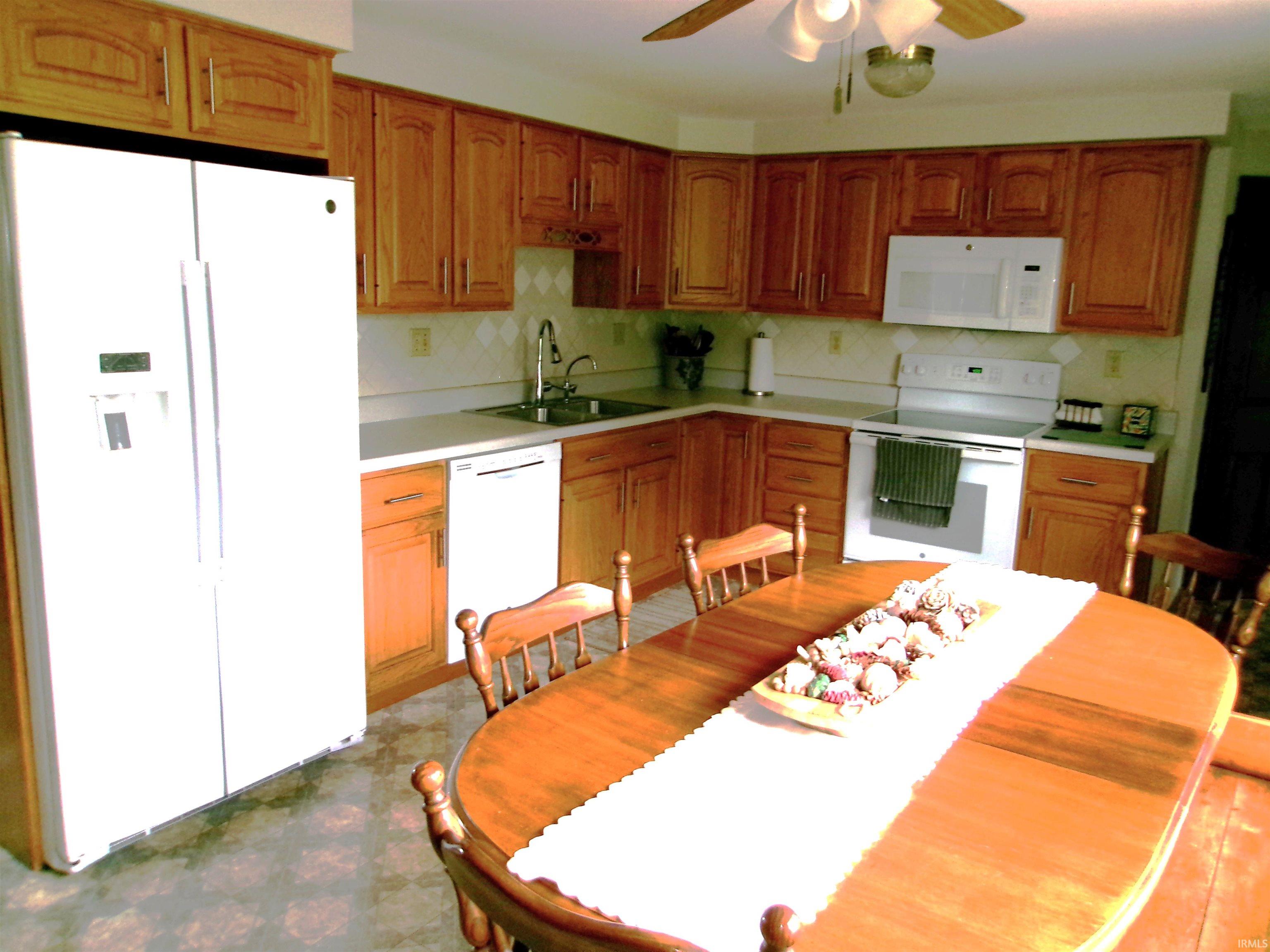 Kitchen featuring wood cabinetry, white appliances, light countertops, and a ceiling fan