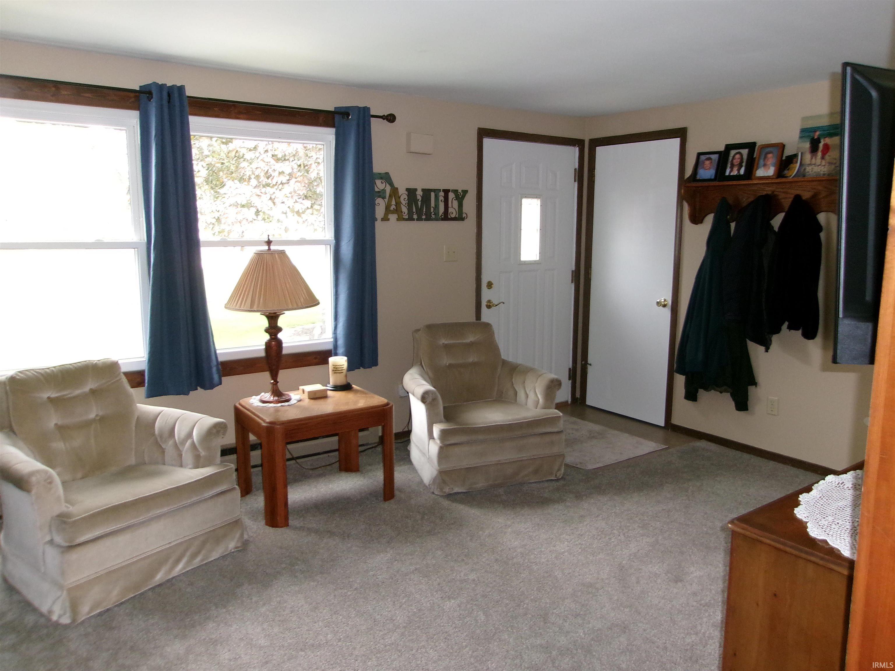 Living area featuring two windows with wood trim, a paneled entry door with a rectangular glass insert, neutral wall paint, and grey carpet flooring