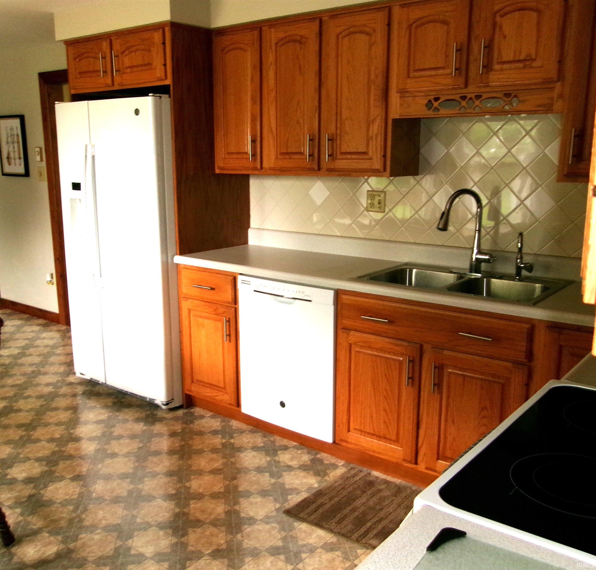 Kitchen featuring wood cabinetry, white countertops, a tile backsplash, and a double basin stainless steel sink with a gooseneck faucet