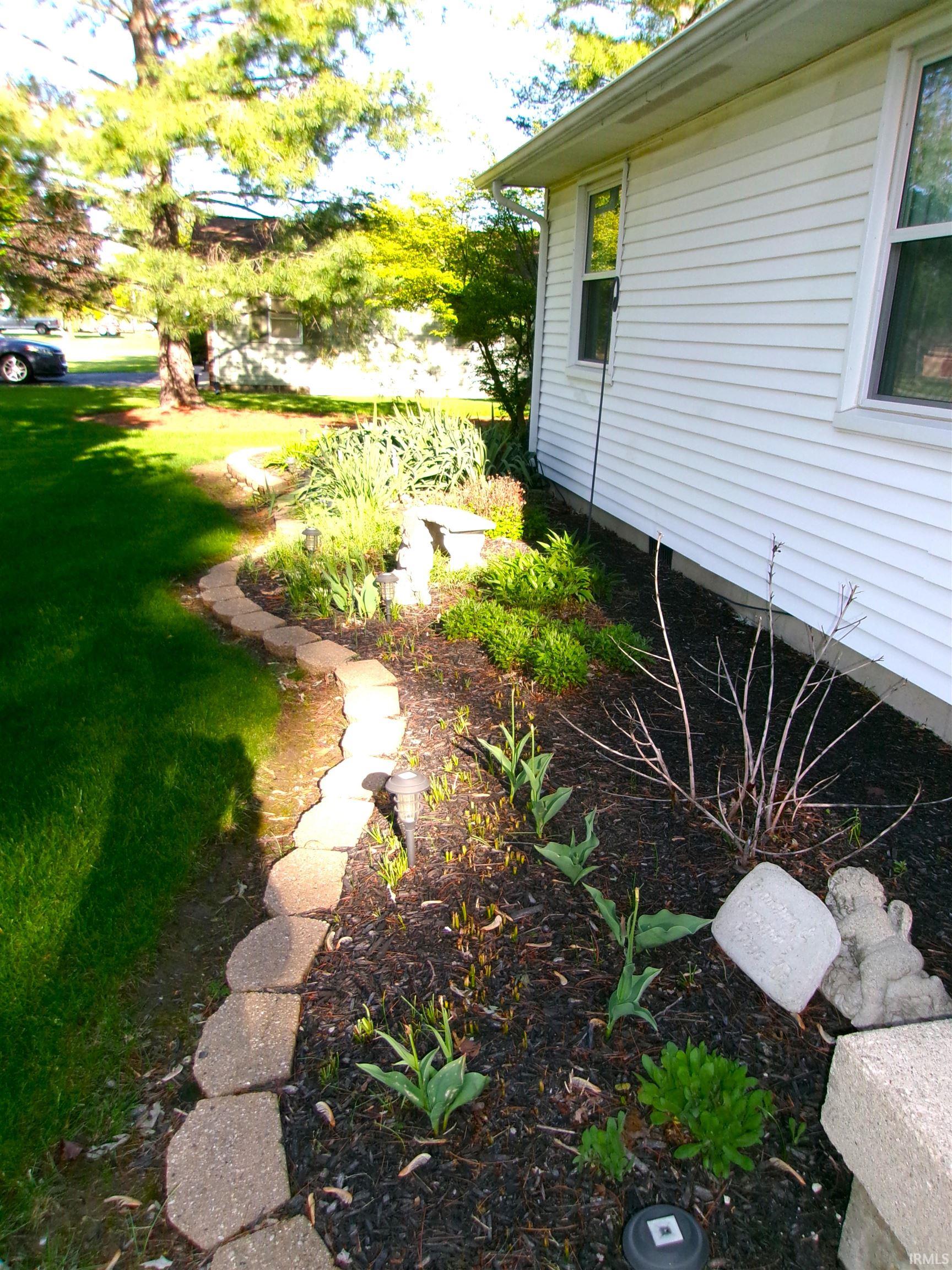White vinyl siding exterior with a landscaped garden bed featuring a concrete block border