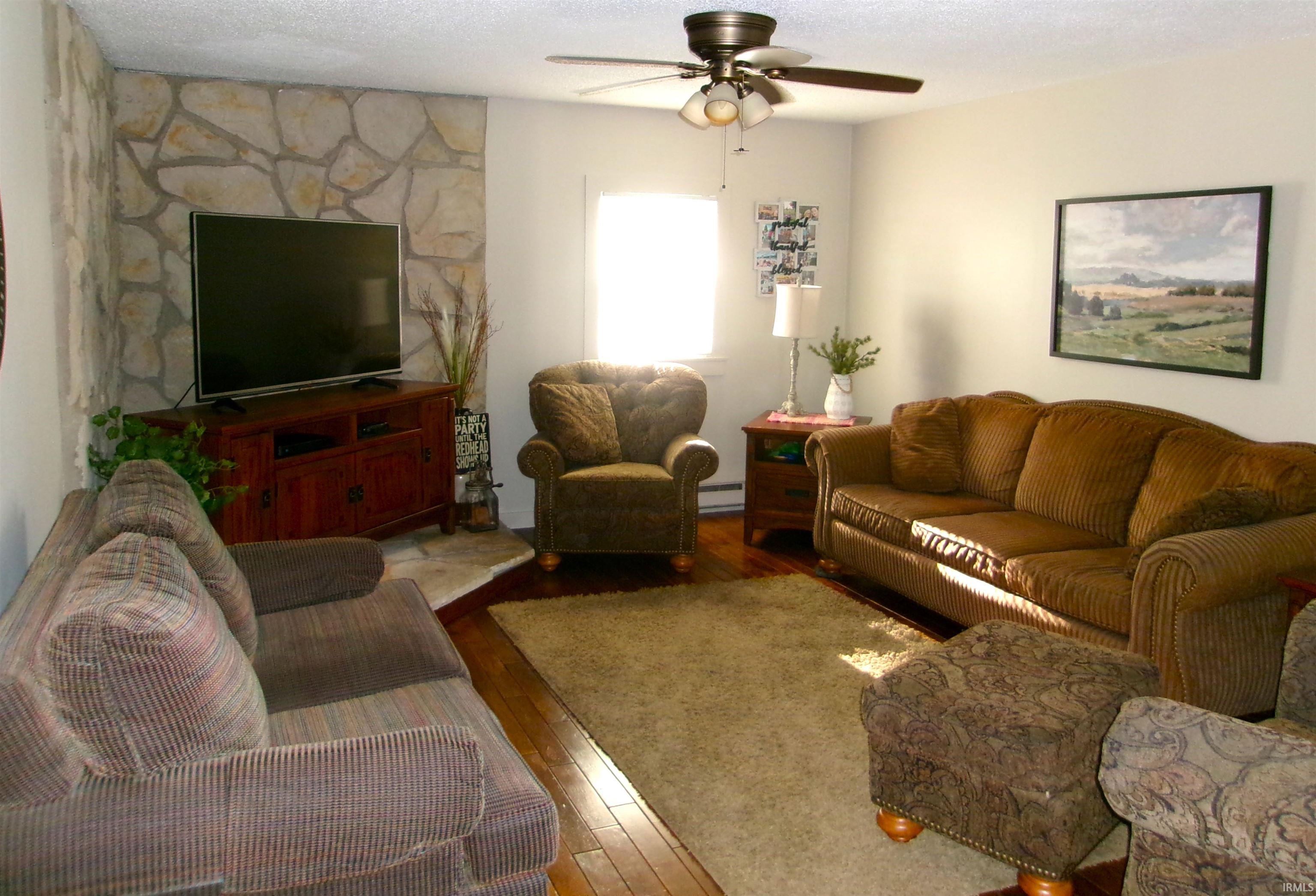 Living area featuring an accent wall with stacked stone, wood-finish flooring, a ceiling fan, and a single window