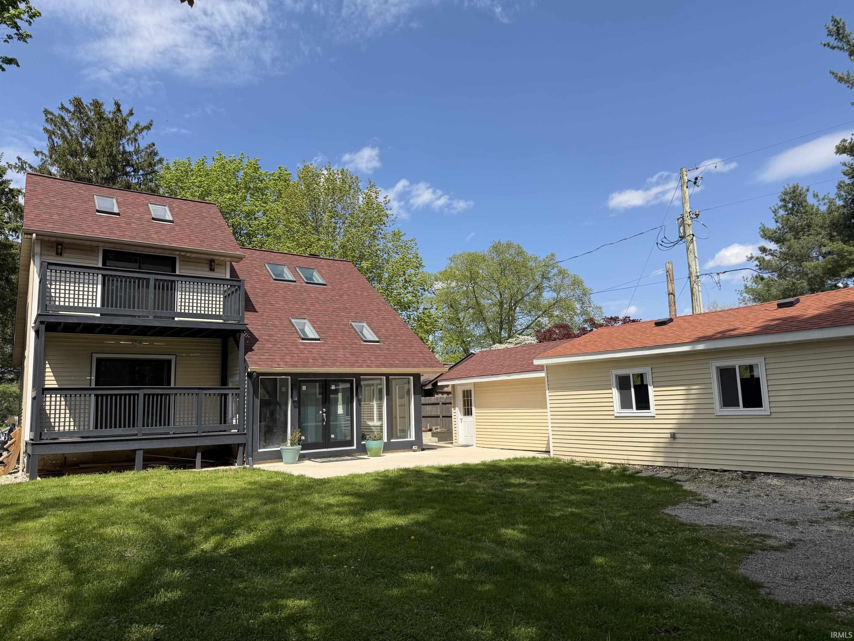 Contemporary-style exterior featuring durable vinyl siding, a multi-level deck with dark railings, a red shingle roof with multiple skylights, and a detached garage with complementary siding