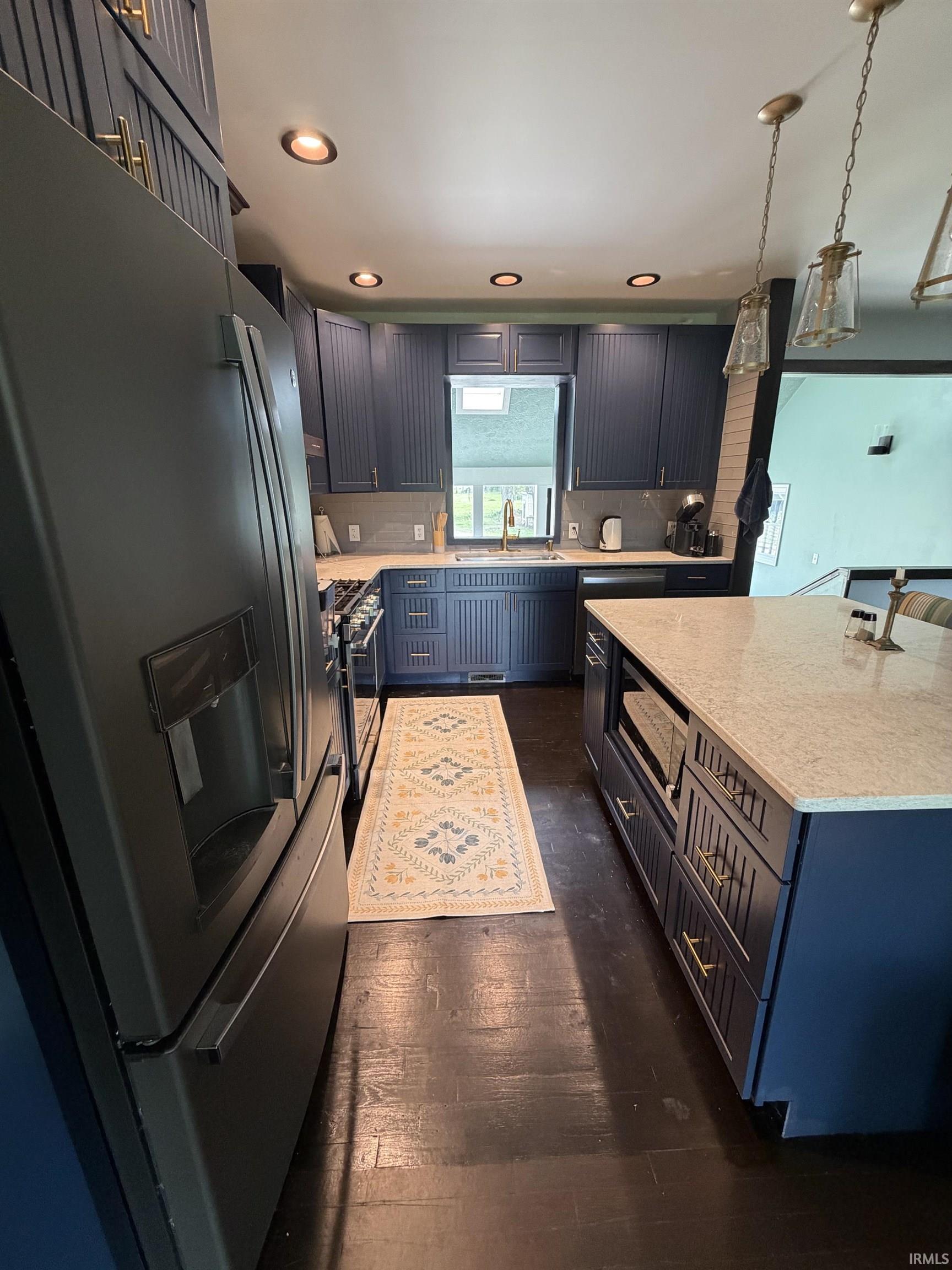 Kitchen featuring dark wood-finish flooring, navy cabinetry with gold-tone hardware, light-toned countertops, and a window above the sink