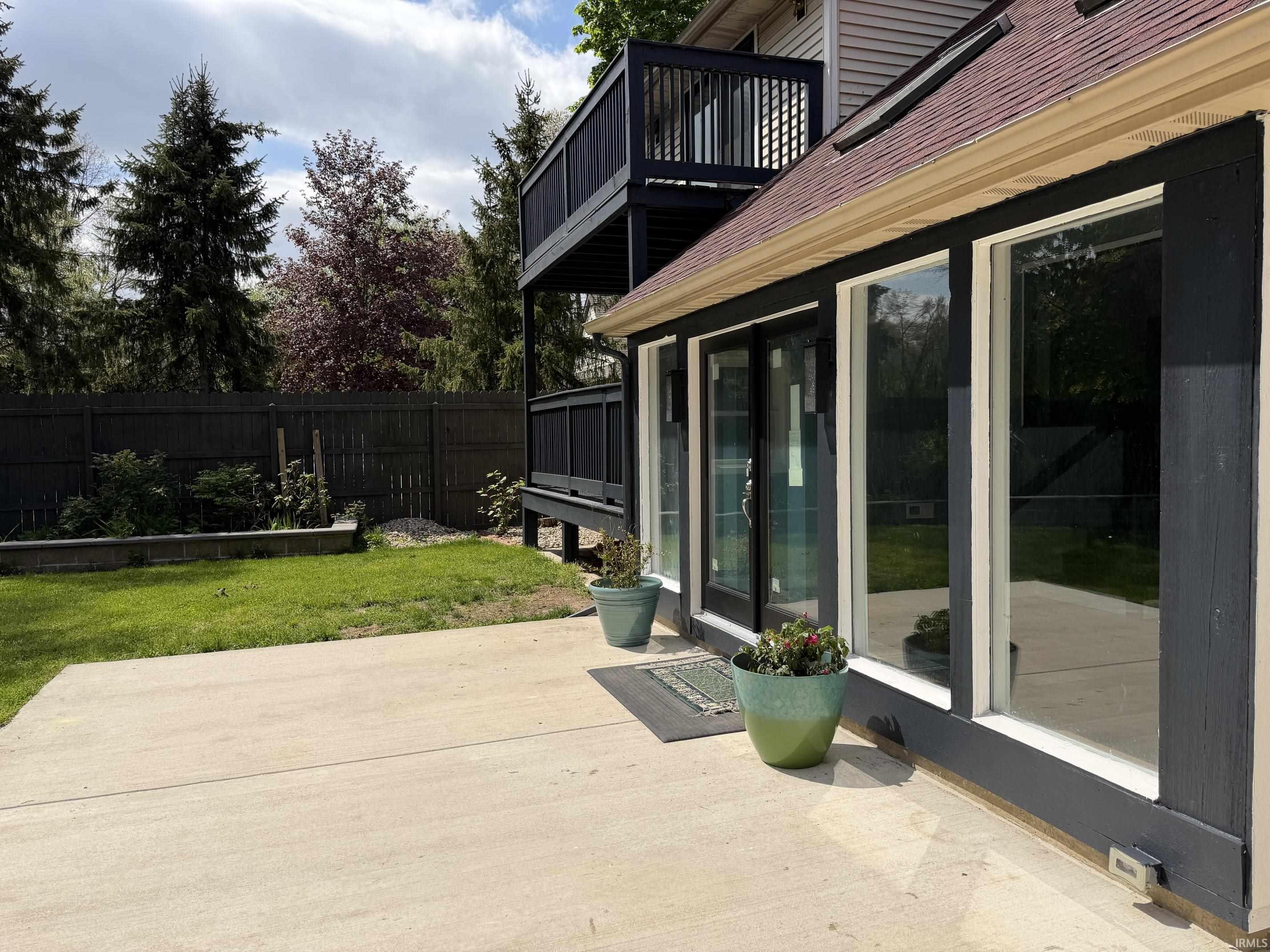 Expansive concrete patio with multiple glass sliding doors, dark exterior trim, and a second-story balcony