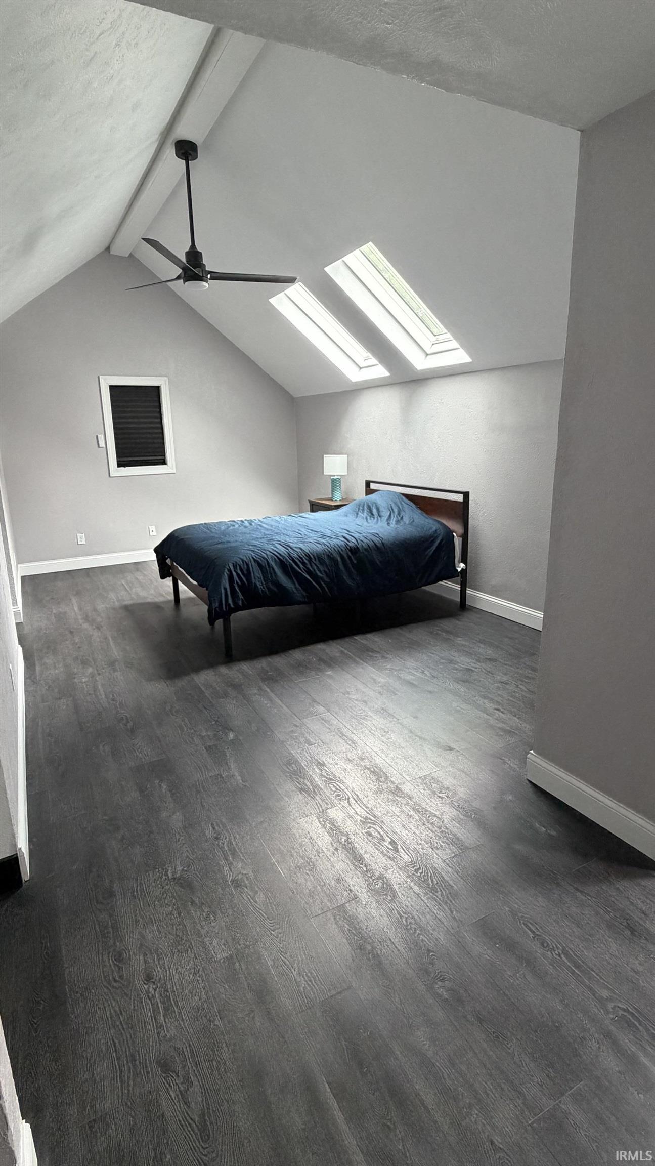 Vaulted ceiling room featuring wood-finish flooring, a ceiling fan, and two skylights