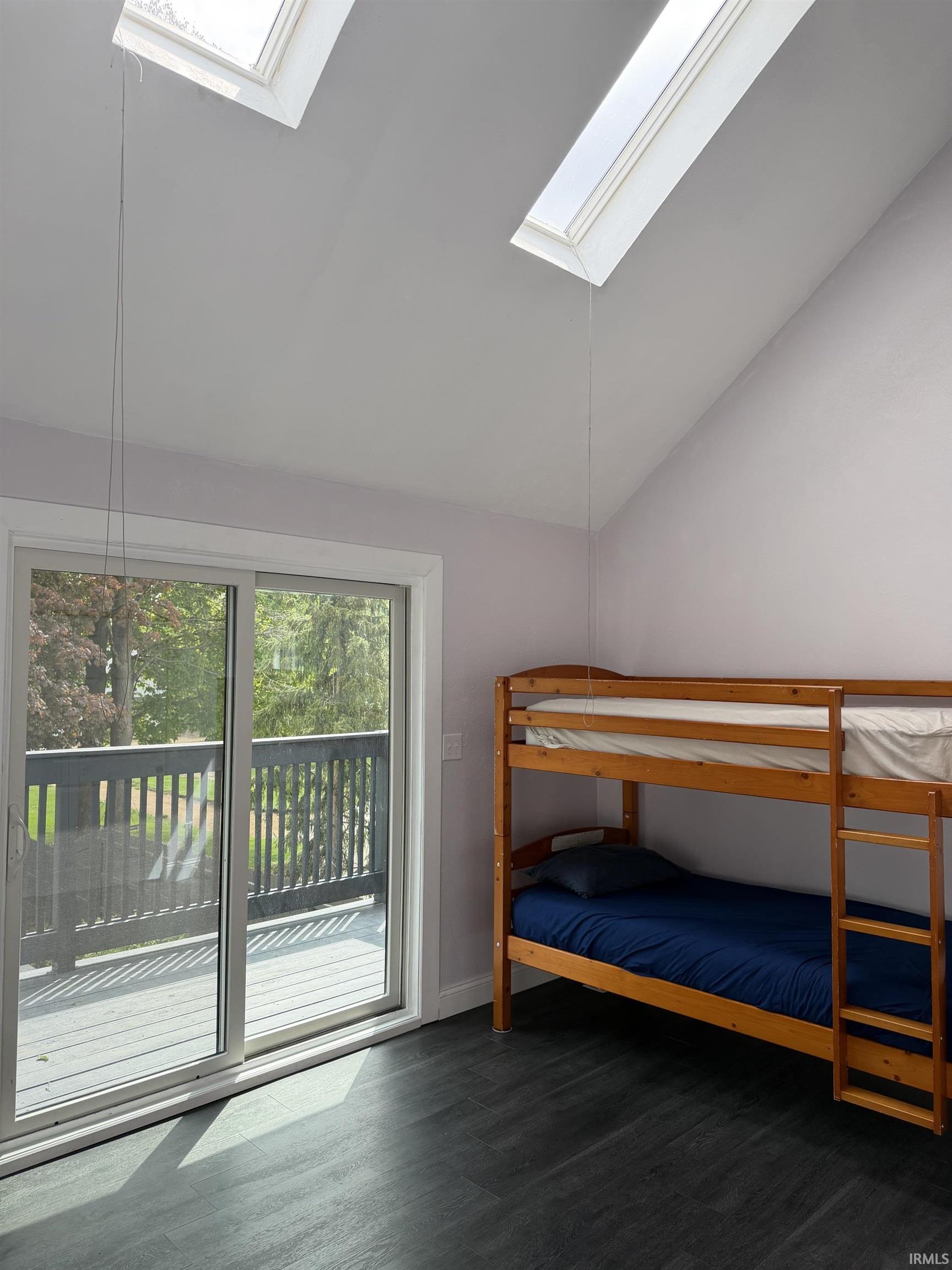 Room with dark wood-finish flooring, featuring two skylights, a vaulted ceiling, and light-toned walls
