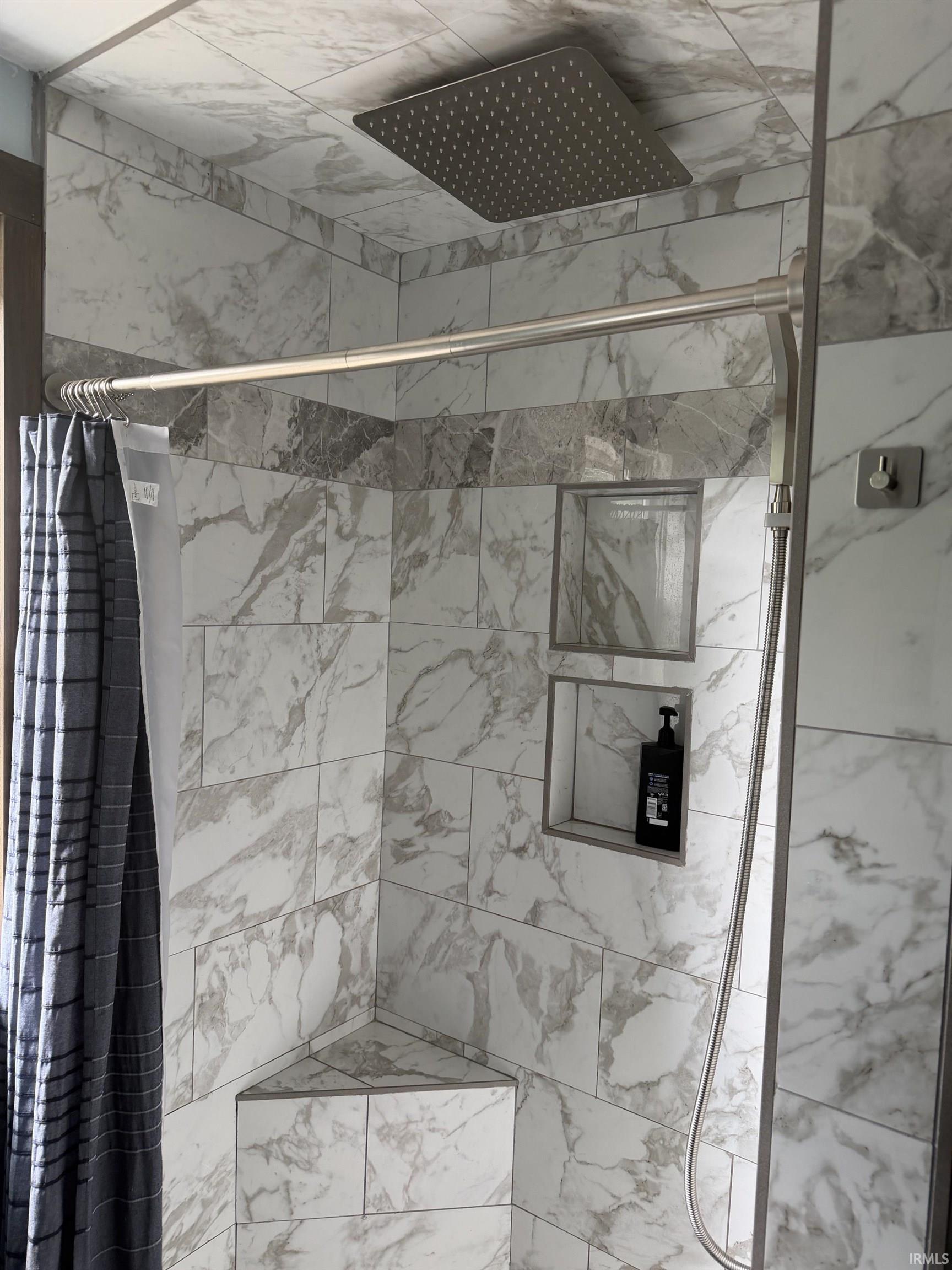 Shower enclosure featuring marble-look tiling and a ceiling-mounted rainfall showerhead