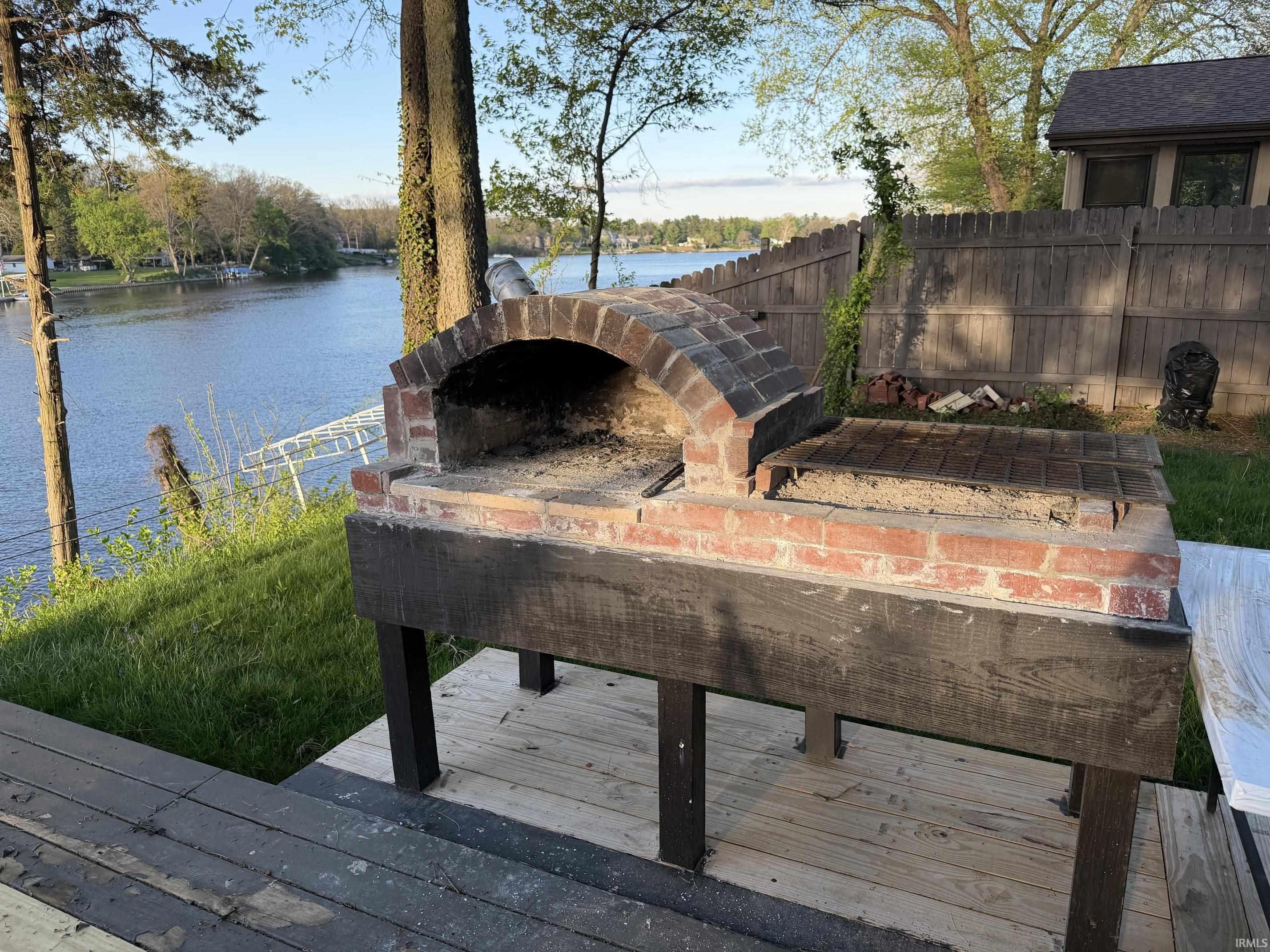 Outdoor brick oven with an integrated grill, positioned on a wood-finish deck
