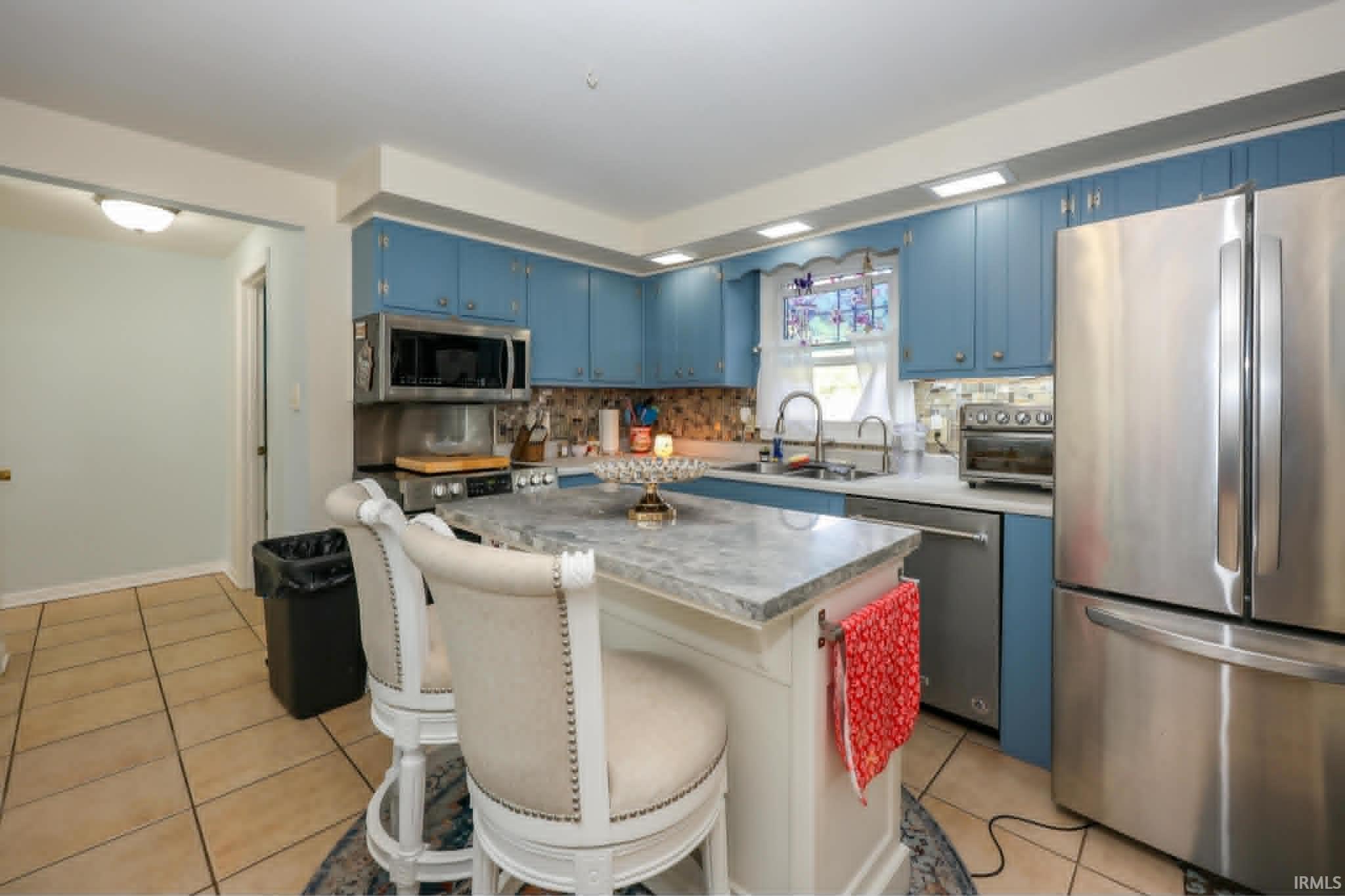 Kitchen featuring a central island with a light-toned countertop, blue cabinetry, stainless steel appliances, and tiled flooring