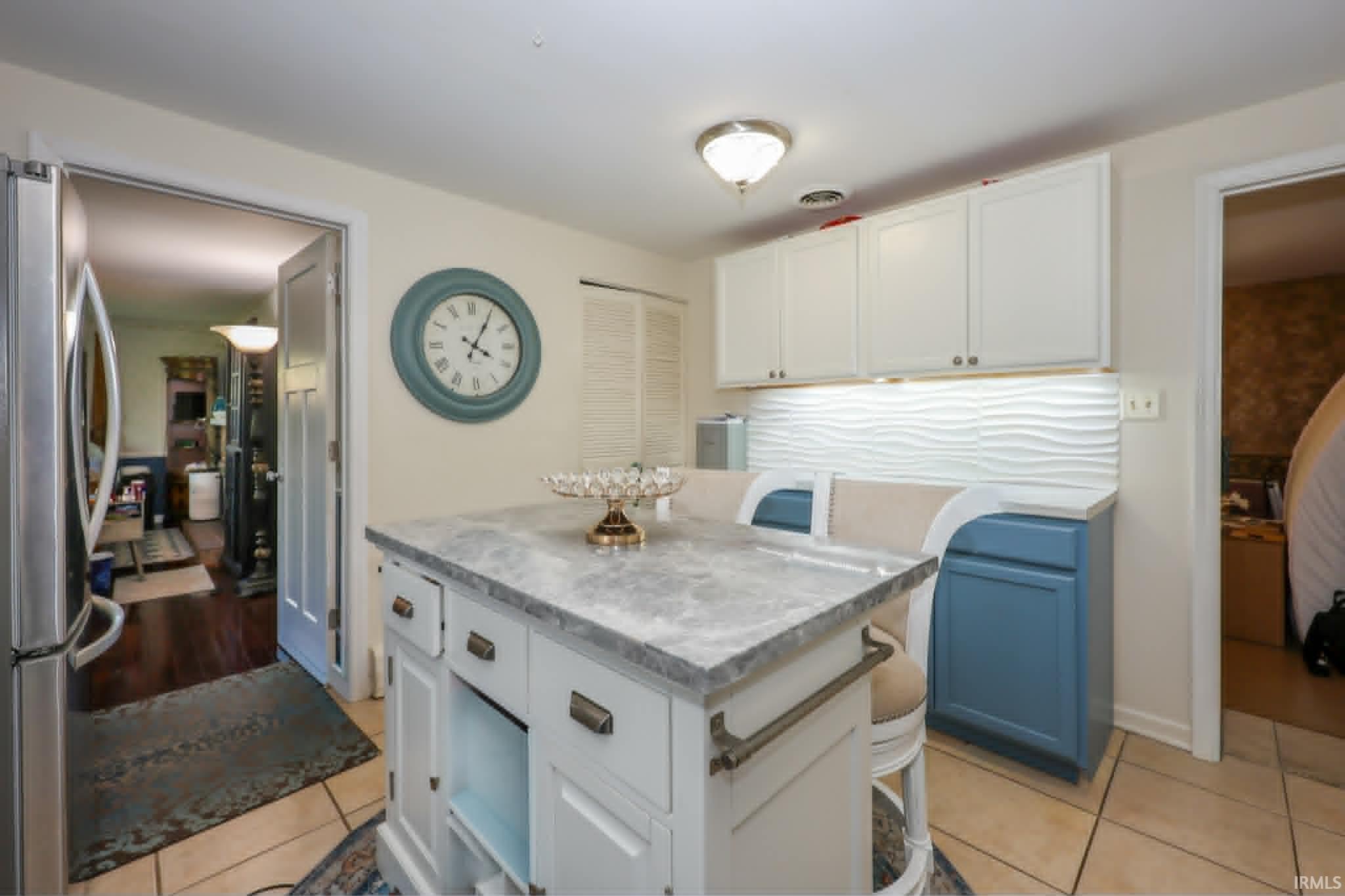 Kitchen featuring a central island with a grey countertop, white cabinetry with bronze hardware, and tile flooring